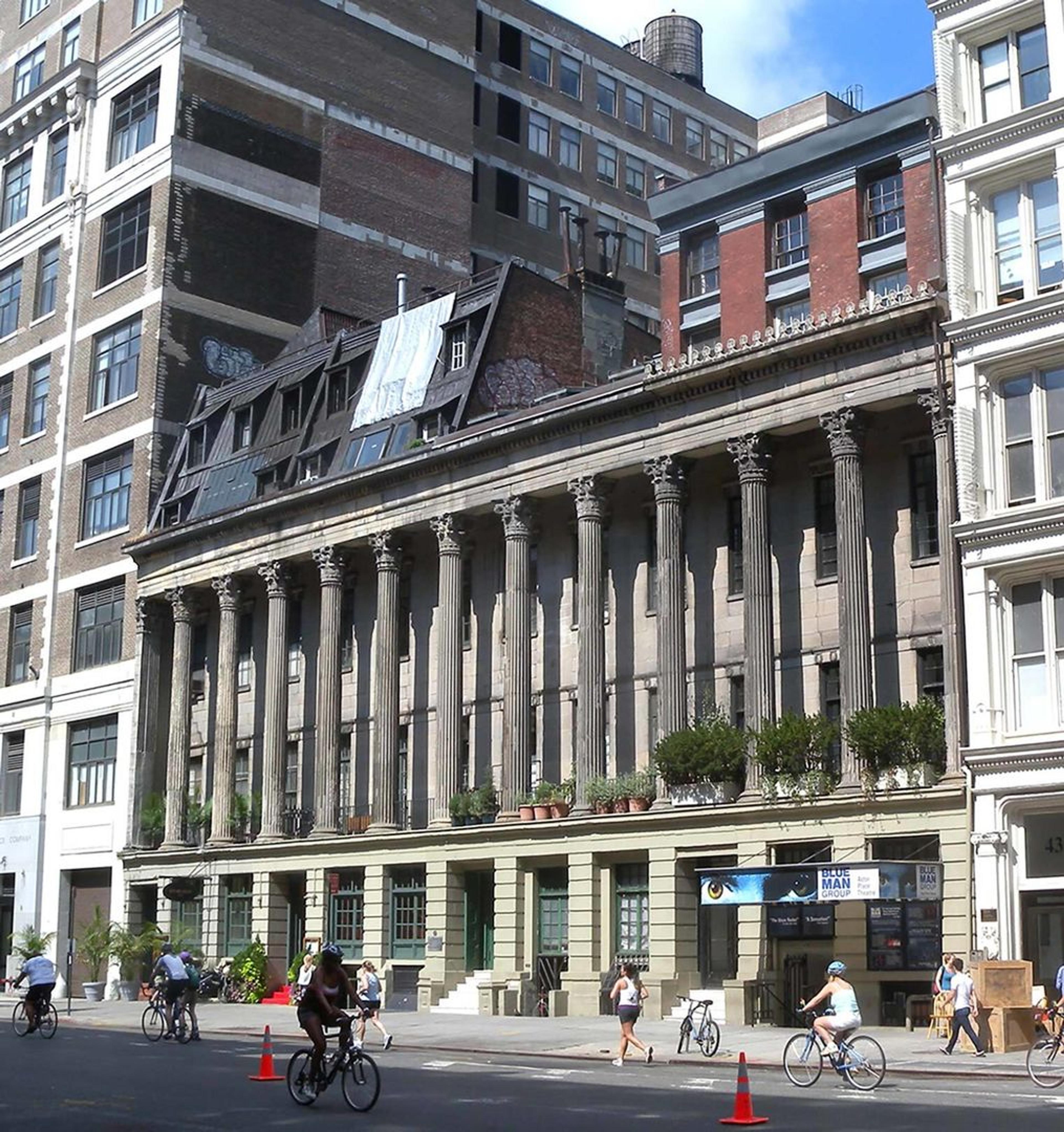 A contemporary photo of Colonnade Row, a regal building with Neoclassical columns surrounded by modern buildings
