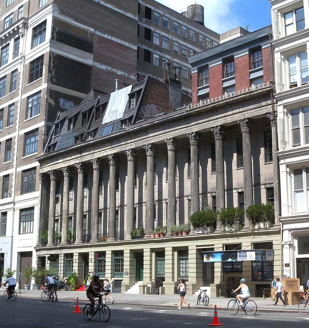 A contemporary photo of Colonnade Row, a regal building with Neoclassical columns surrounded by modern buildings