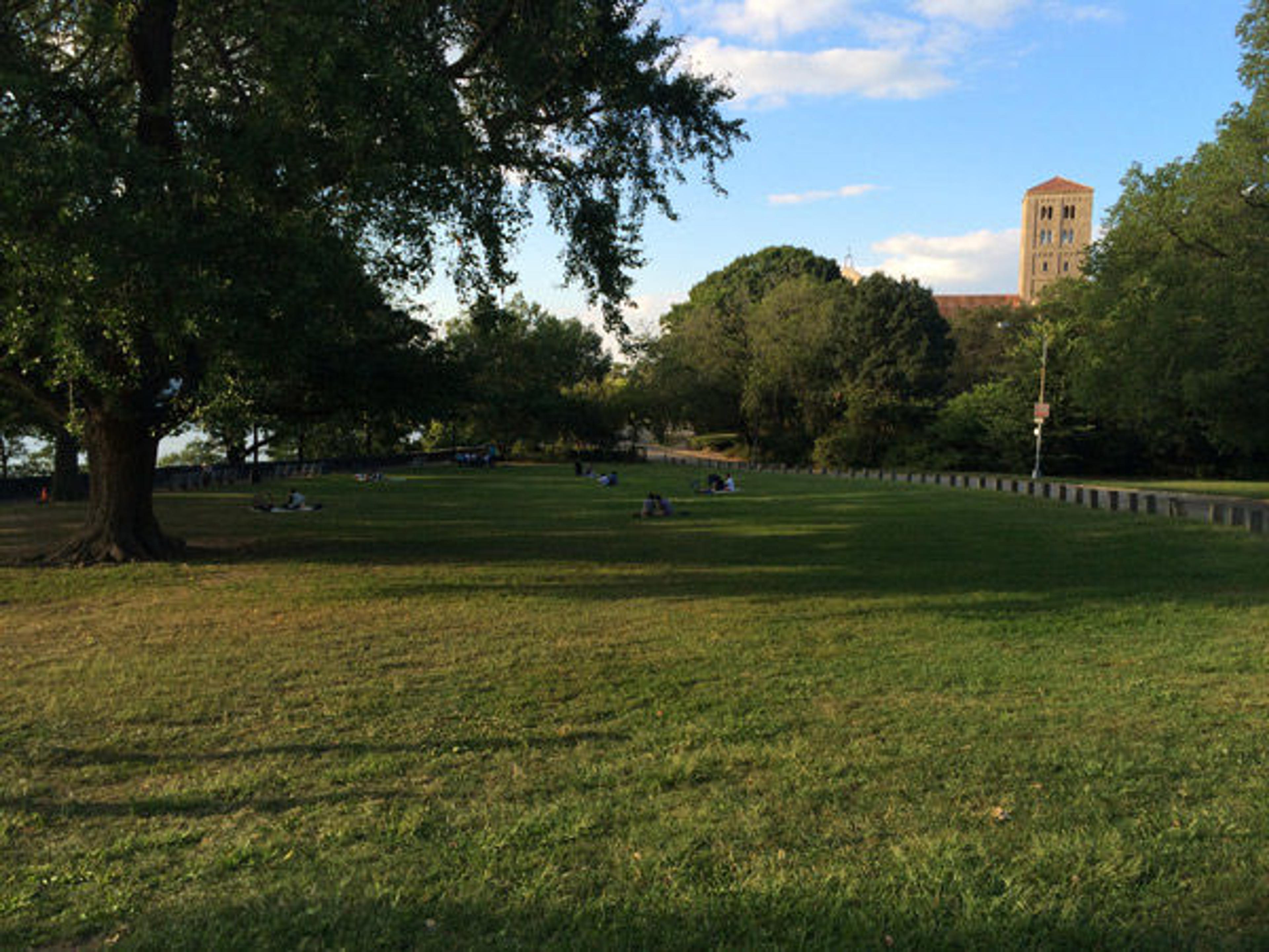 People enjoying a late summer afternoon in Fort Tryon Park with The Cloisters in the background