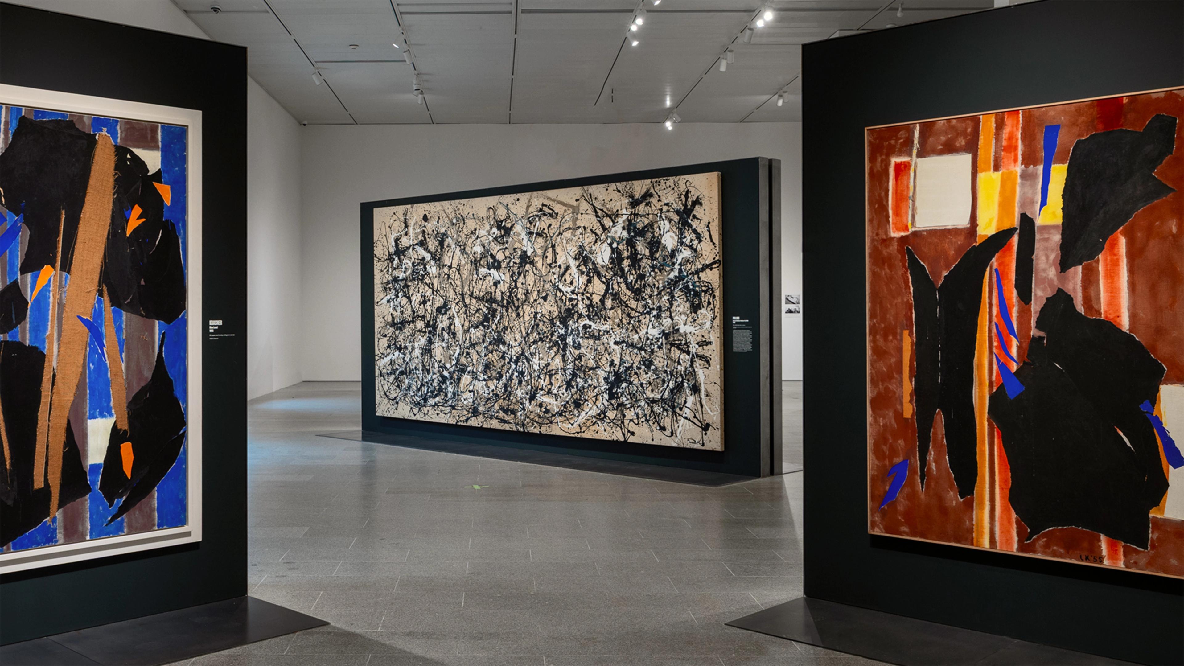 A quiet modern gallery displays three abstract paintings: bold black-and-blue forms, a dense monochrome canvas, and dramatic red-orange shapes.