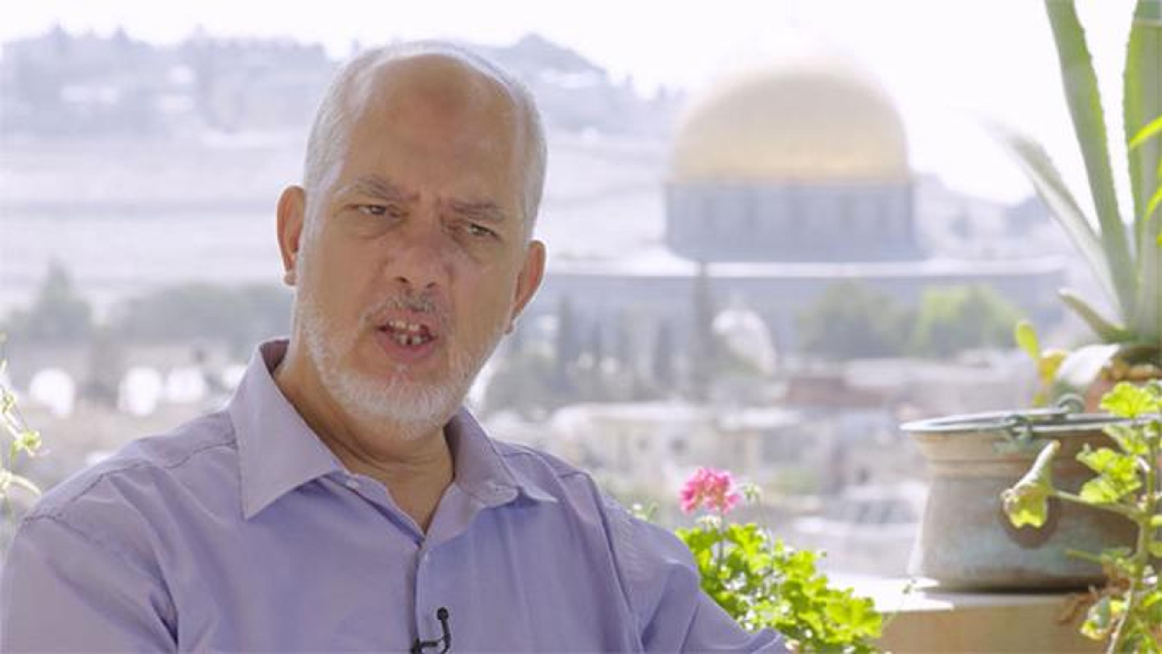 A man speaking with a view of a mosque in the distance