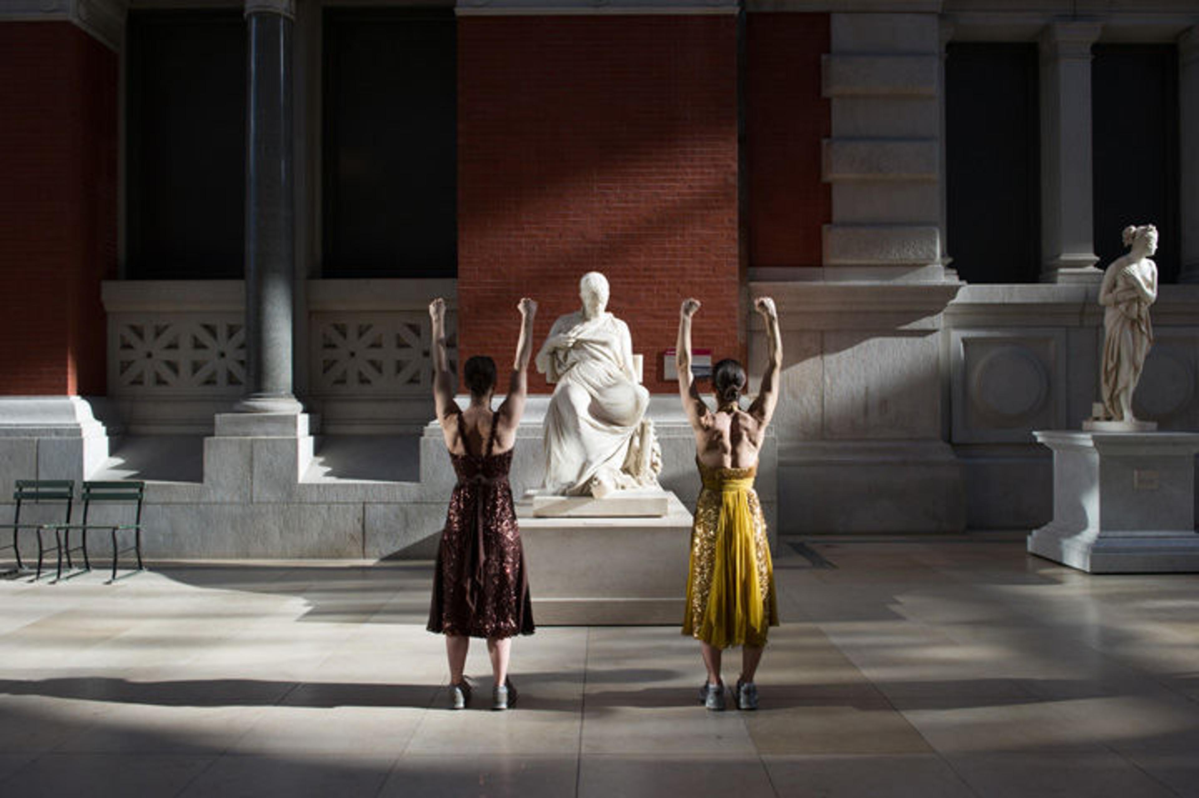 Two women stretch in The Met's European sculpture court while bathed in early morning light