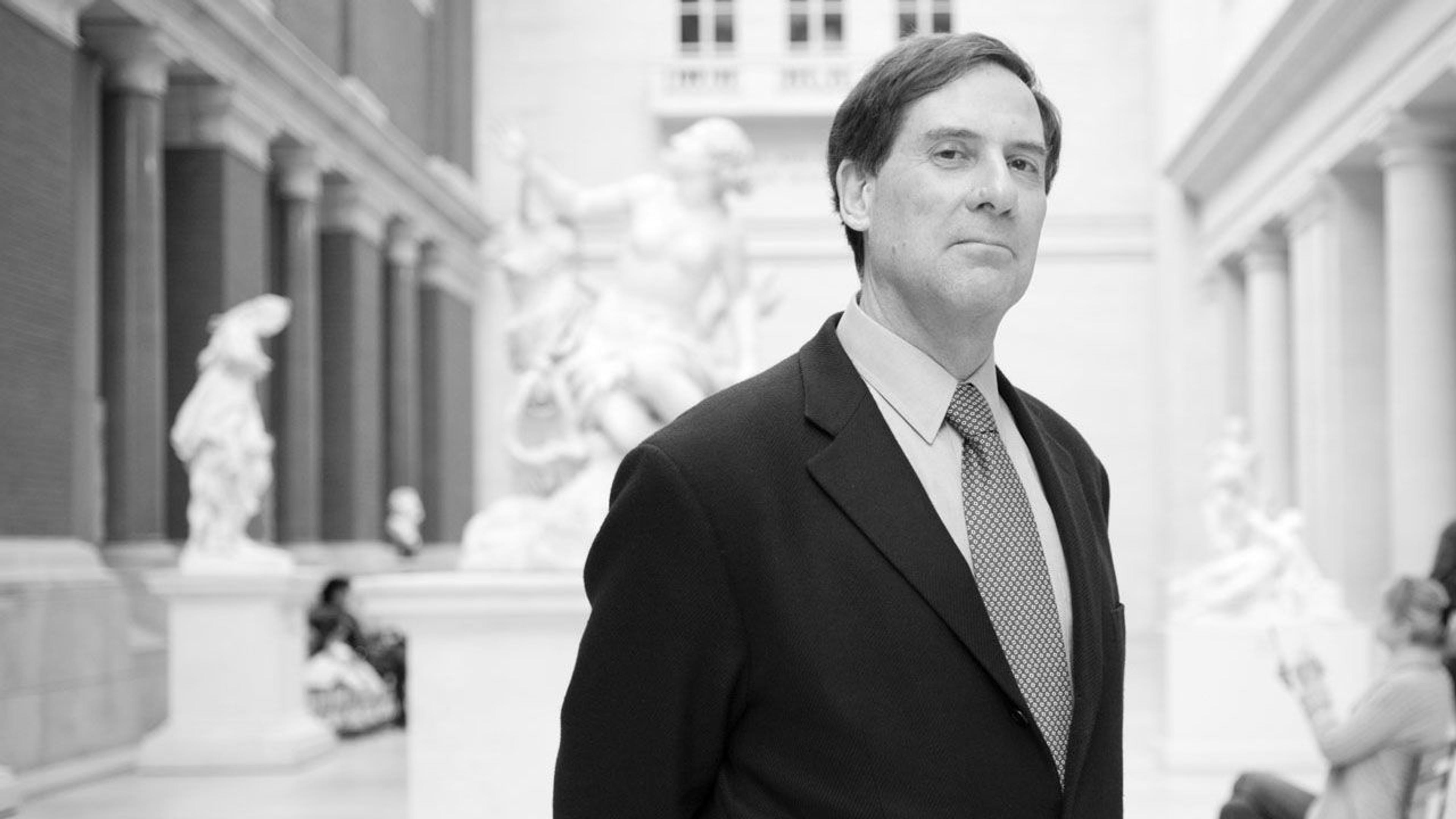 Black and white photograph of curator Ian Wardropper standing in a gallery at The Met