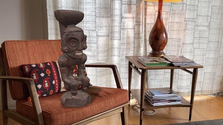 An augmented image of a wood carved Zemí Cohoba Stand in the figure of a deity on a desk