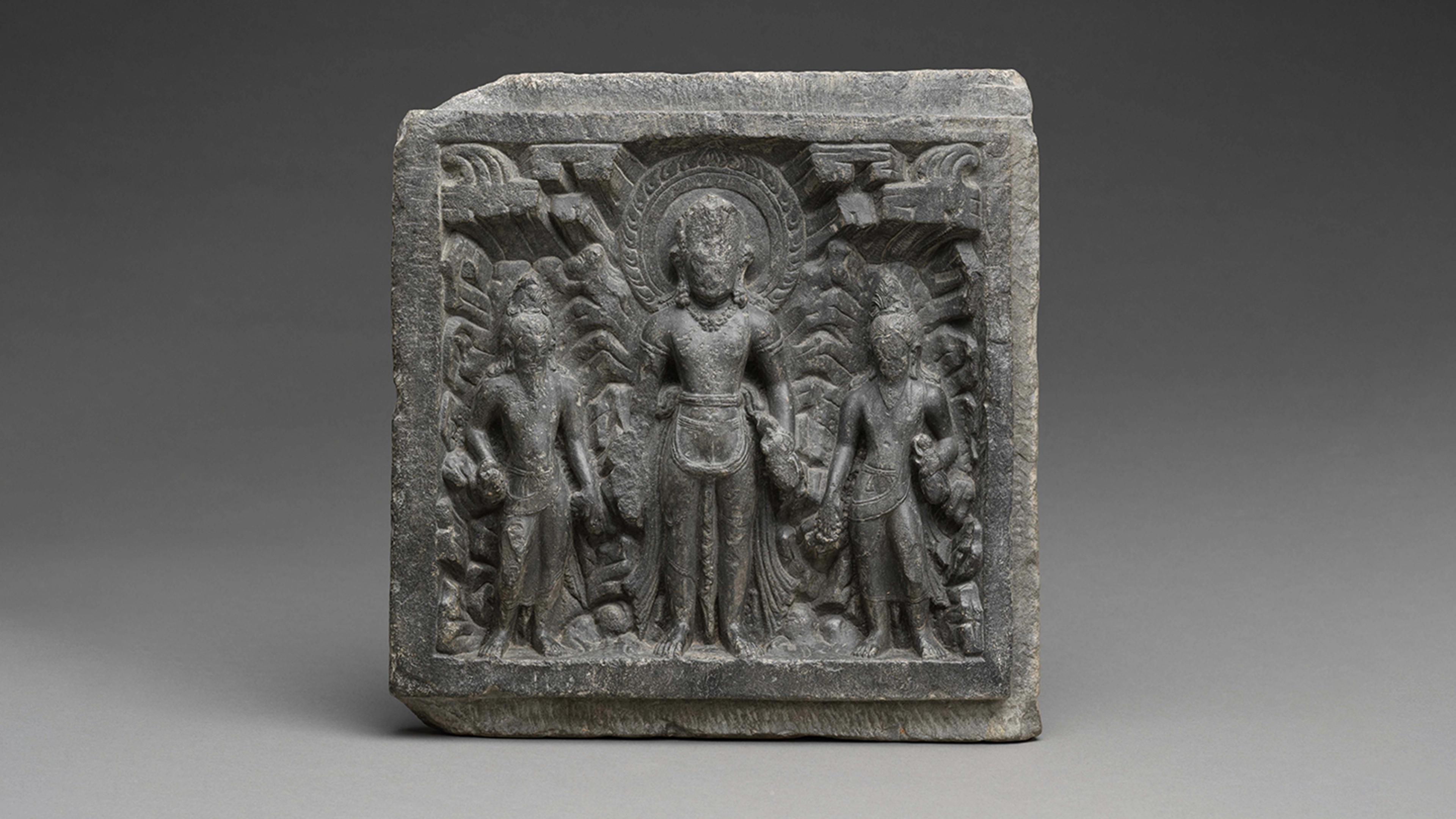 A grey square shaped stone with an engraved scene photographed against a grey background.