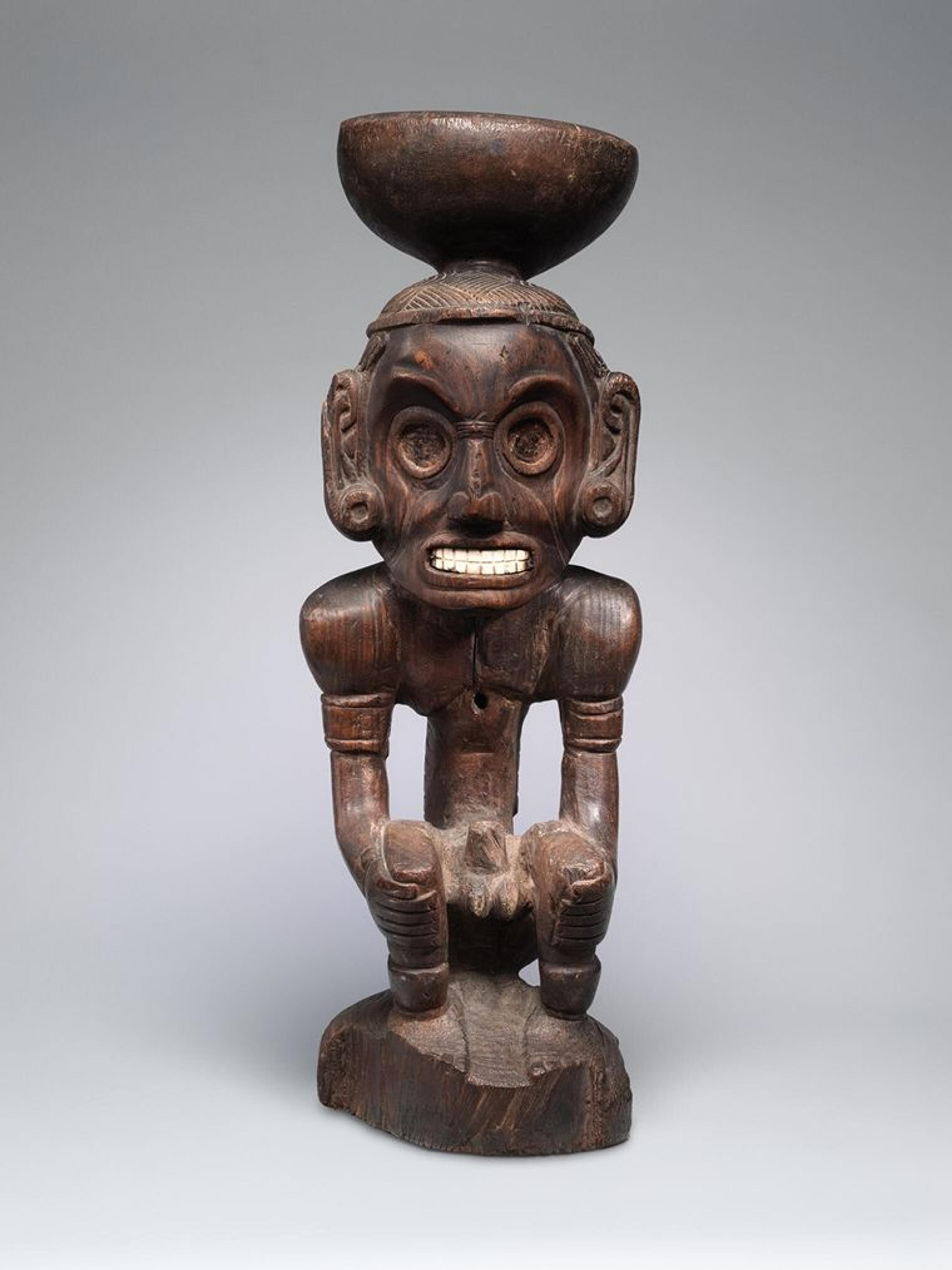 A wooden sculpture of a figure with a stand on its head