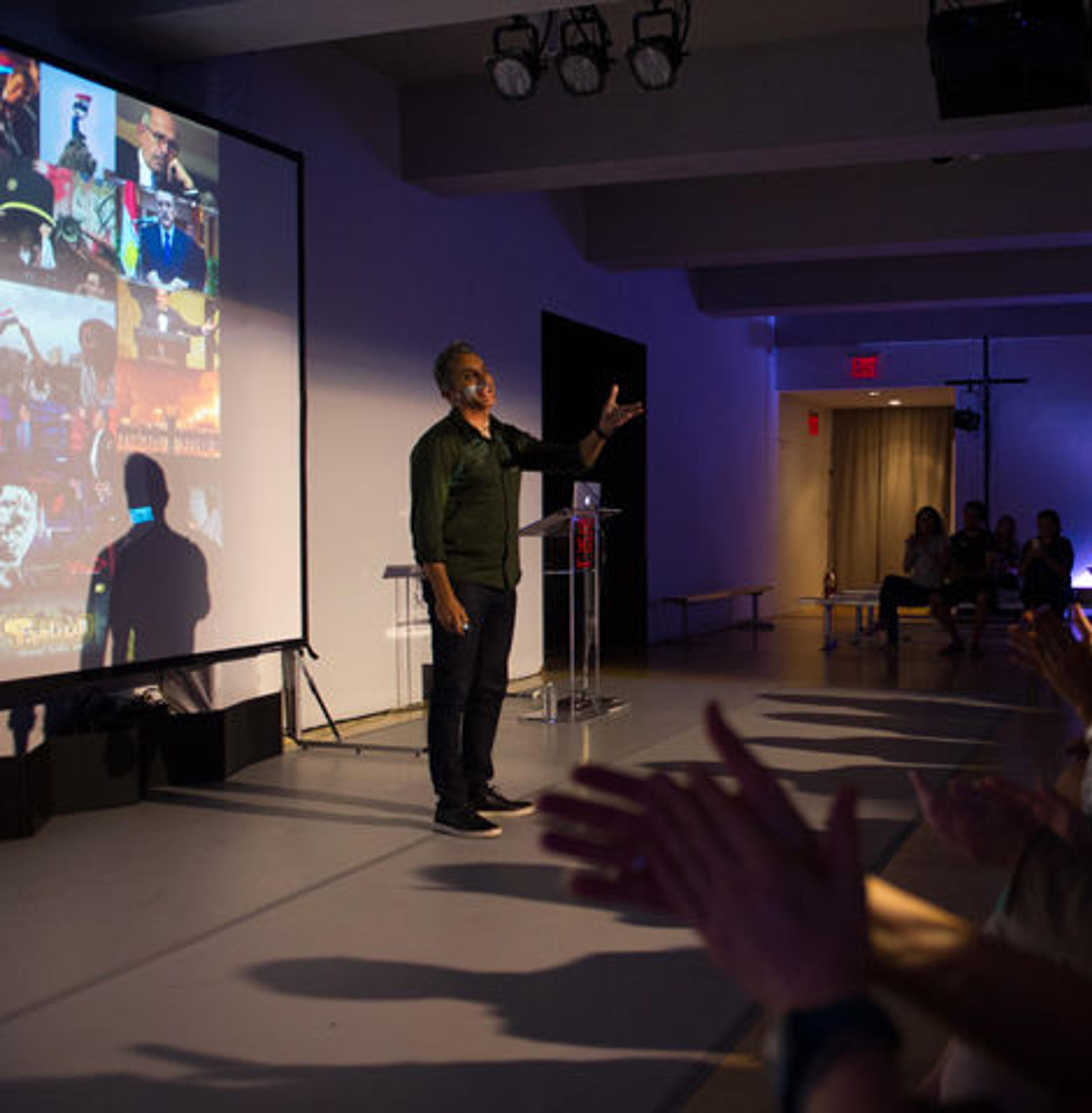 Bassem Youssef speaks to an audience in a small gallery