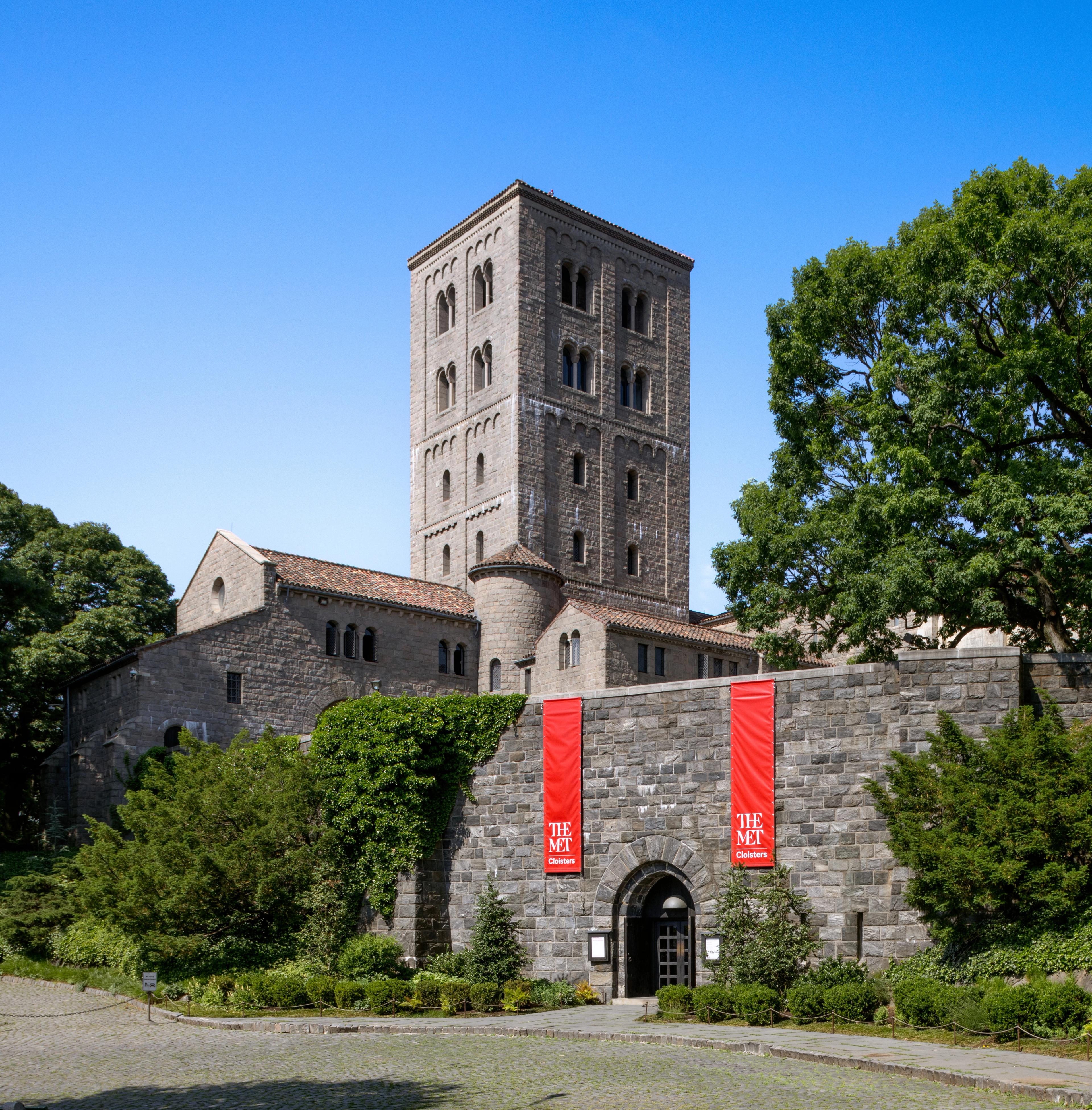 Exterior view of a stone building with a tall square tower, red banners hanging near the entrance