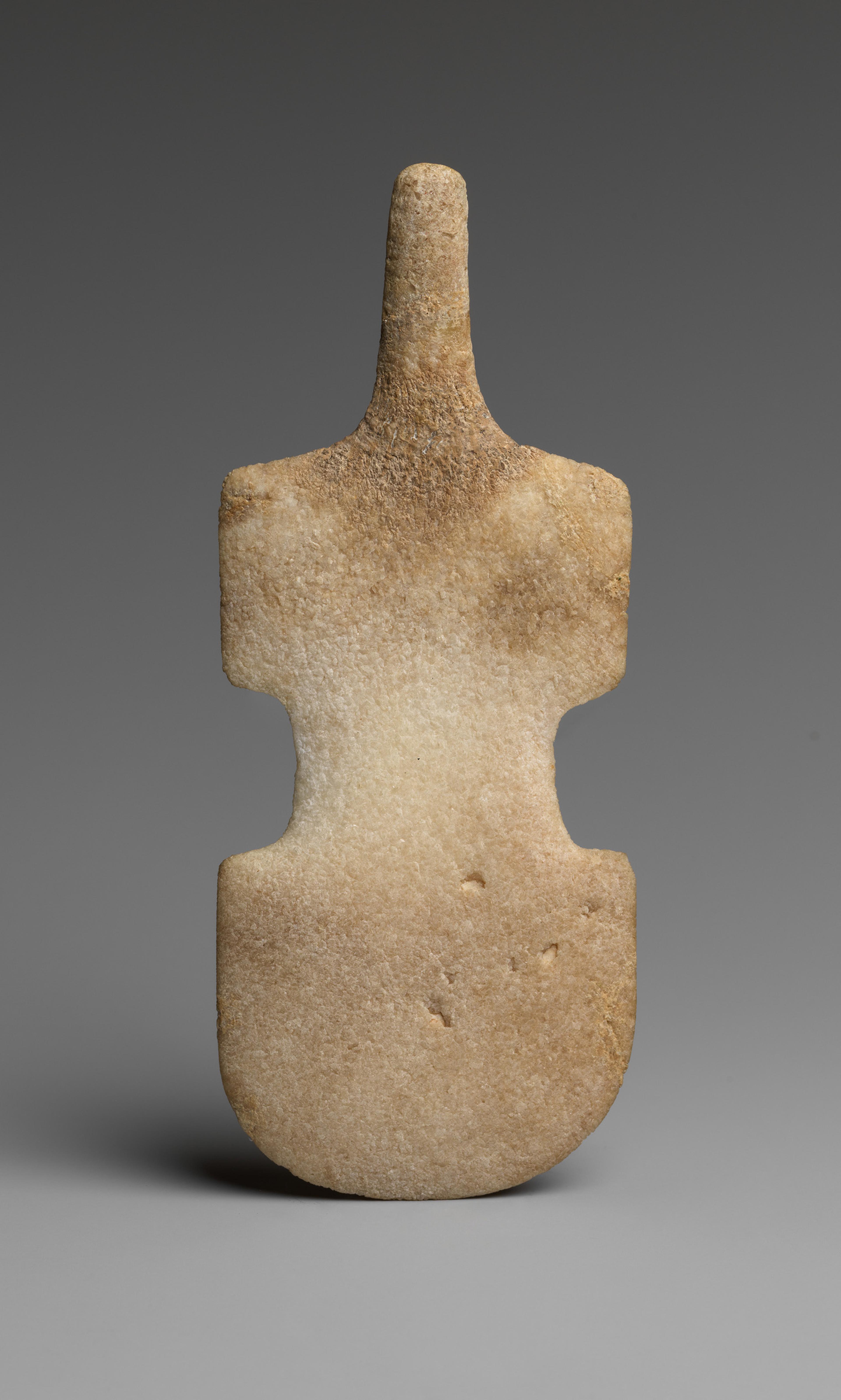 Marble Cycladic figurine with a stylized abstract shape resembling a violin. Its surface has a weathered texture, evoking an ancient, serene aura.