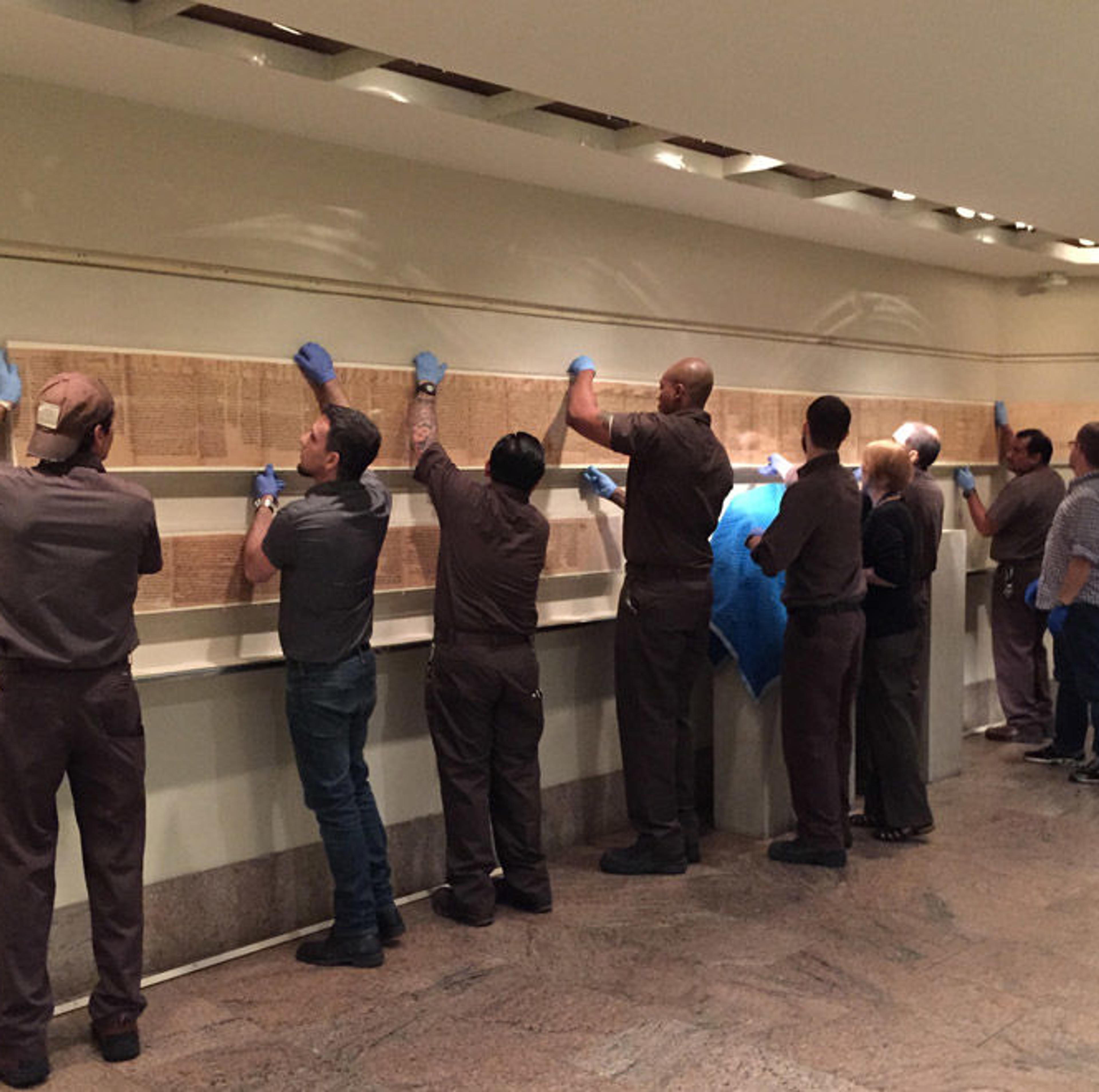 A row of workers holding up a long scroll along a gallery wall.