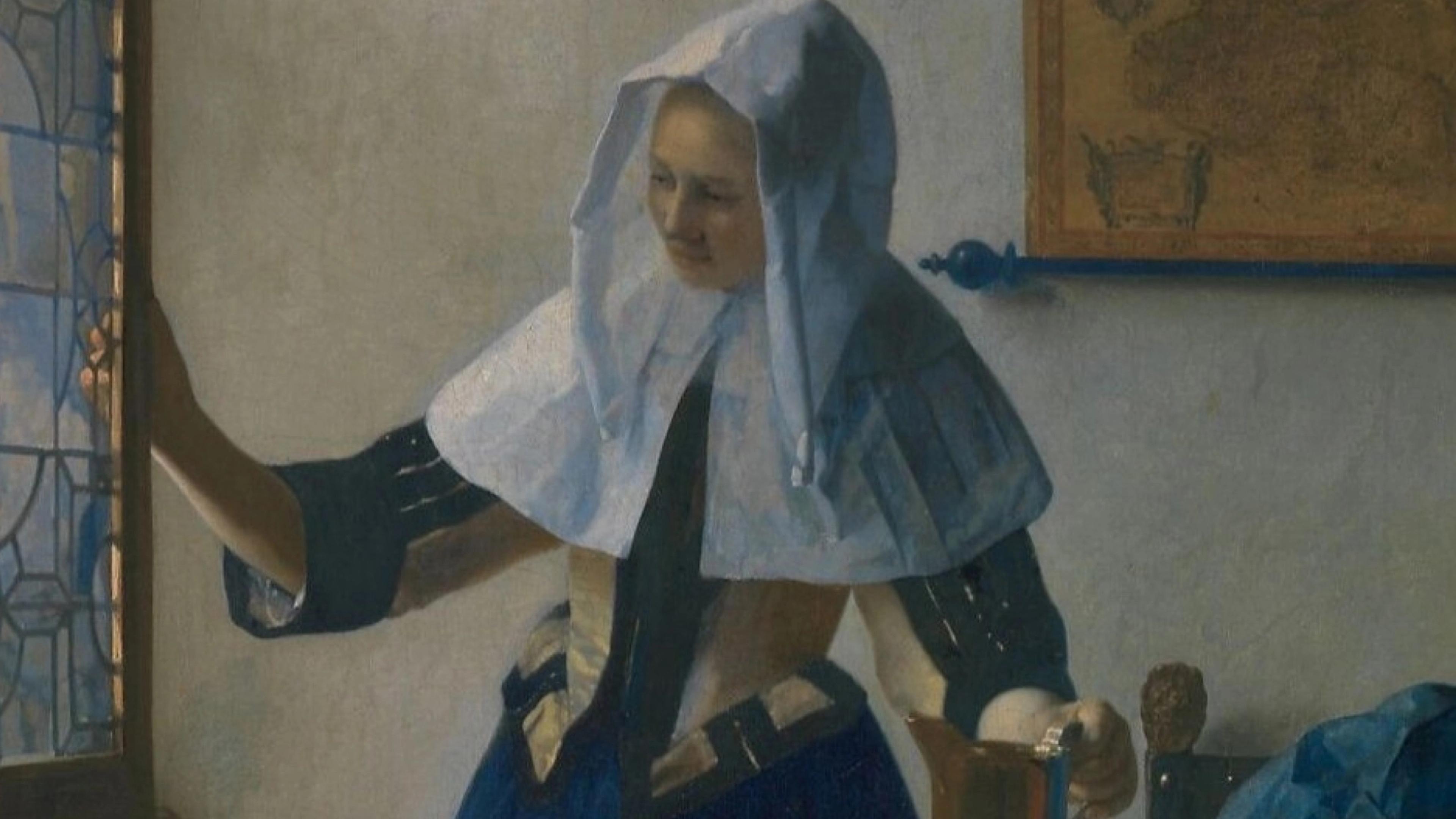 Woman reaching toward a glass panel with a water pitcher in her left hand.