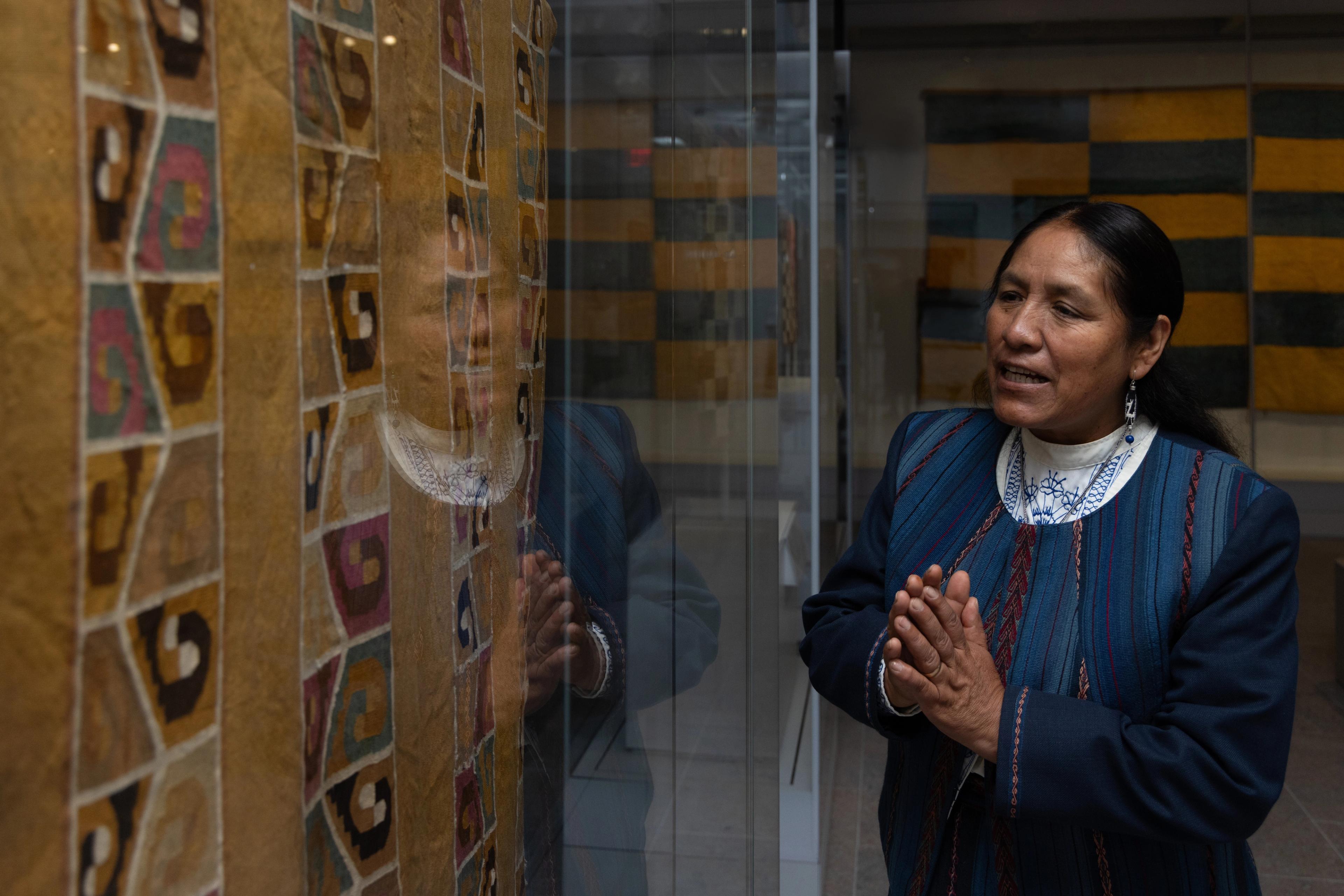 Nilda Callañaupa Alvarez speaking and standing in front of a glass case with a tapestry tunic inside