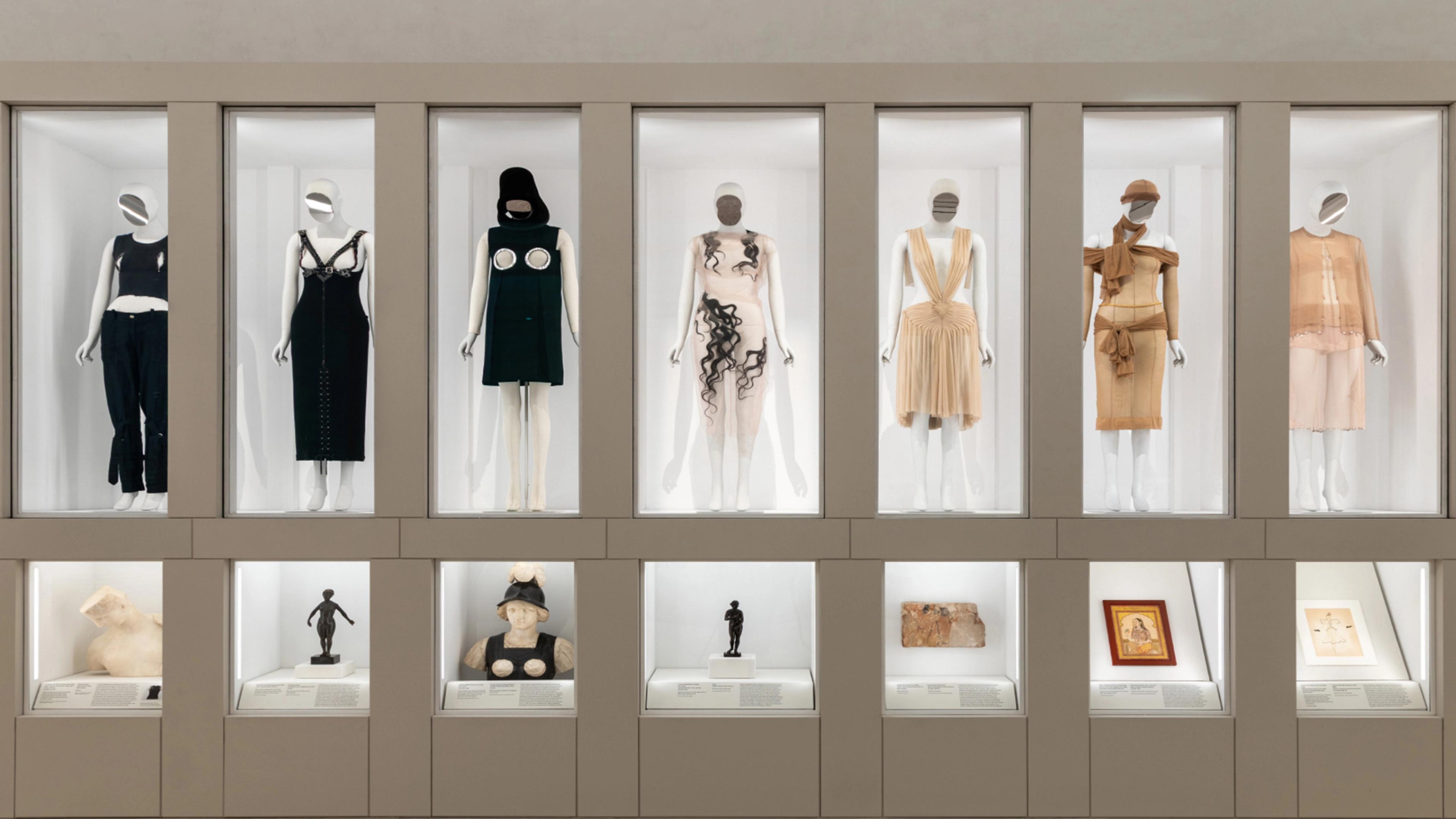 Set of seven mannequins in rectangular displays, each paired with a smaller object placed below.