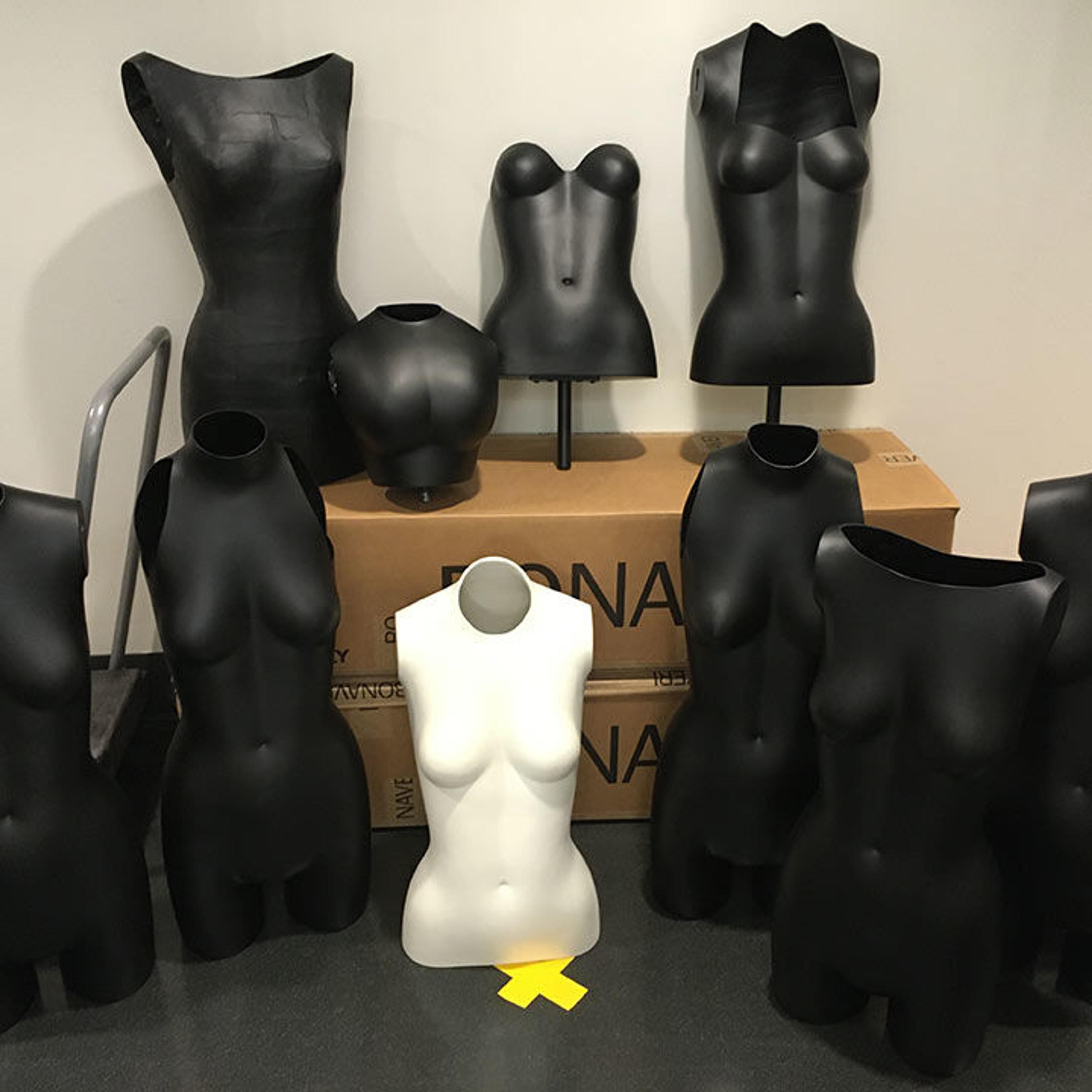 A group of several black and one white mannequin torsos