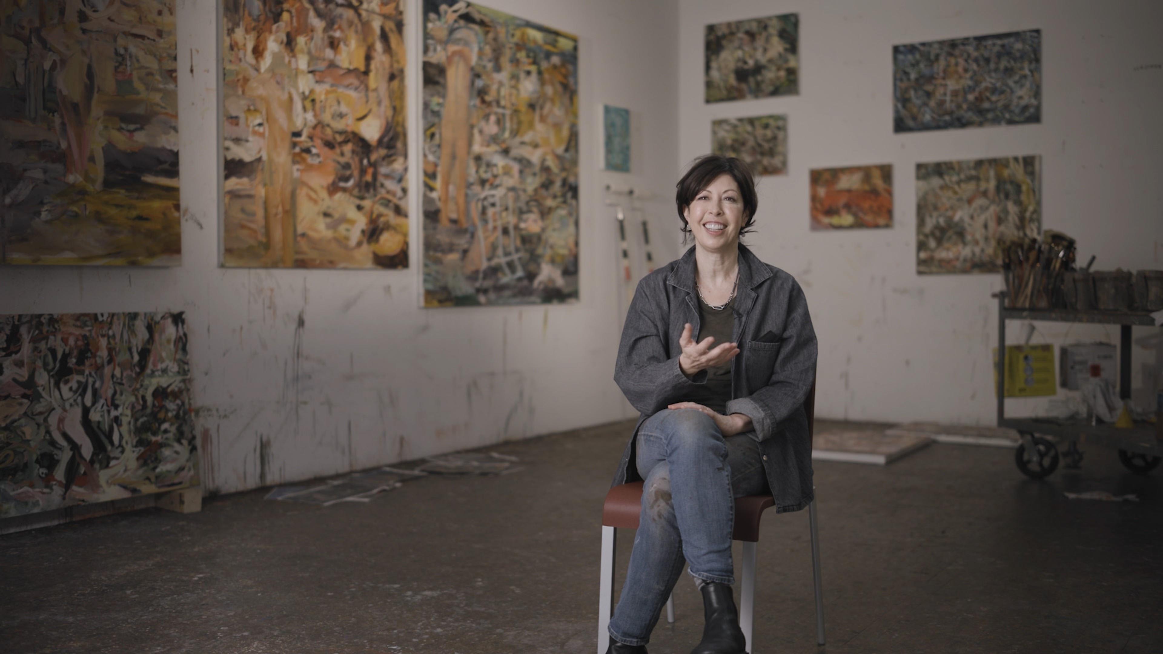 Image of the artist Cecily Brown in her studio surrounded by paintings. 