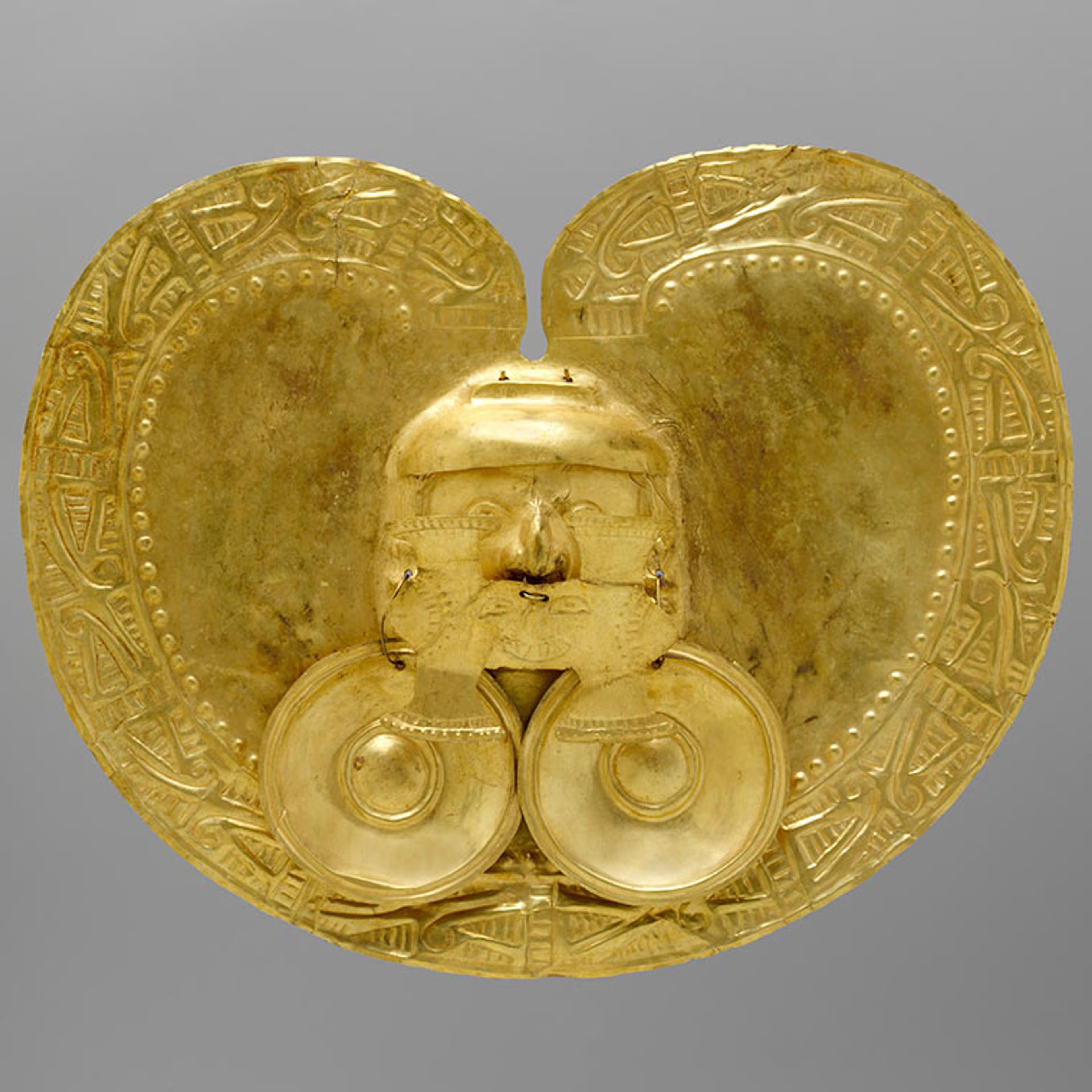A  heart-shaped gold pendant with a relief of a face in the center and two golden circles hanging off of the face's ears.