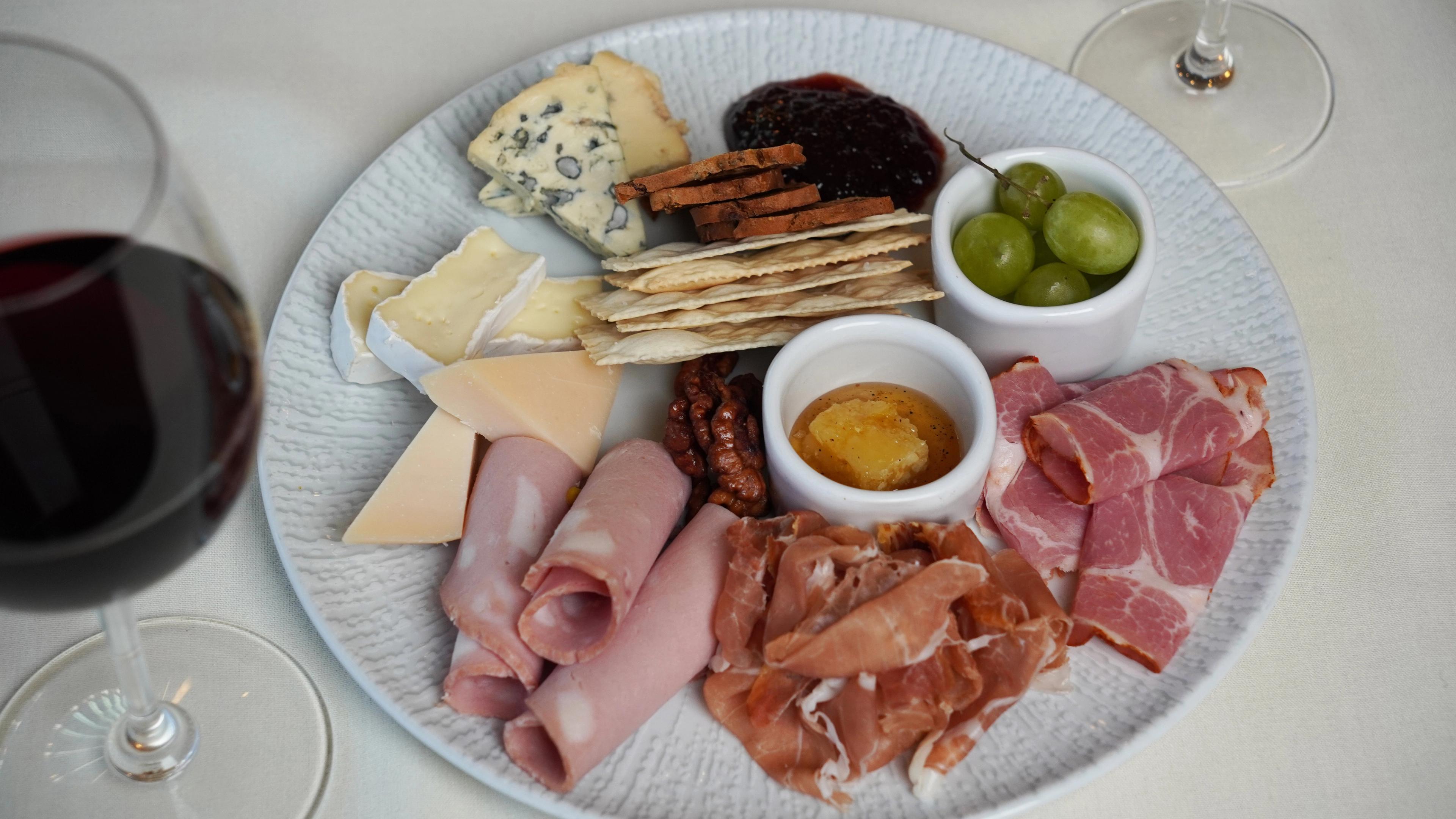 Charcuterie, with meats, cheeses, olives, and crackers, sitting beside a glass of red wine. 