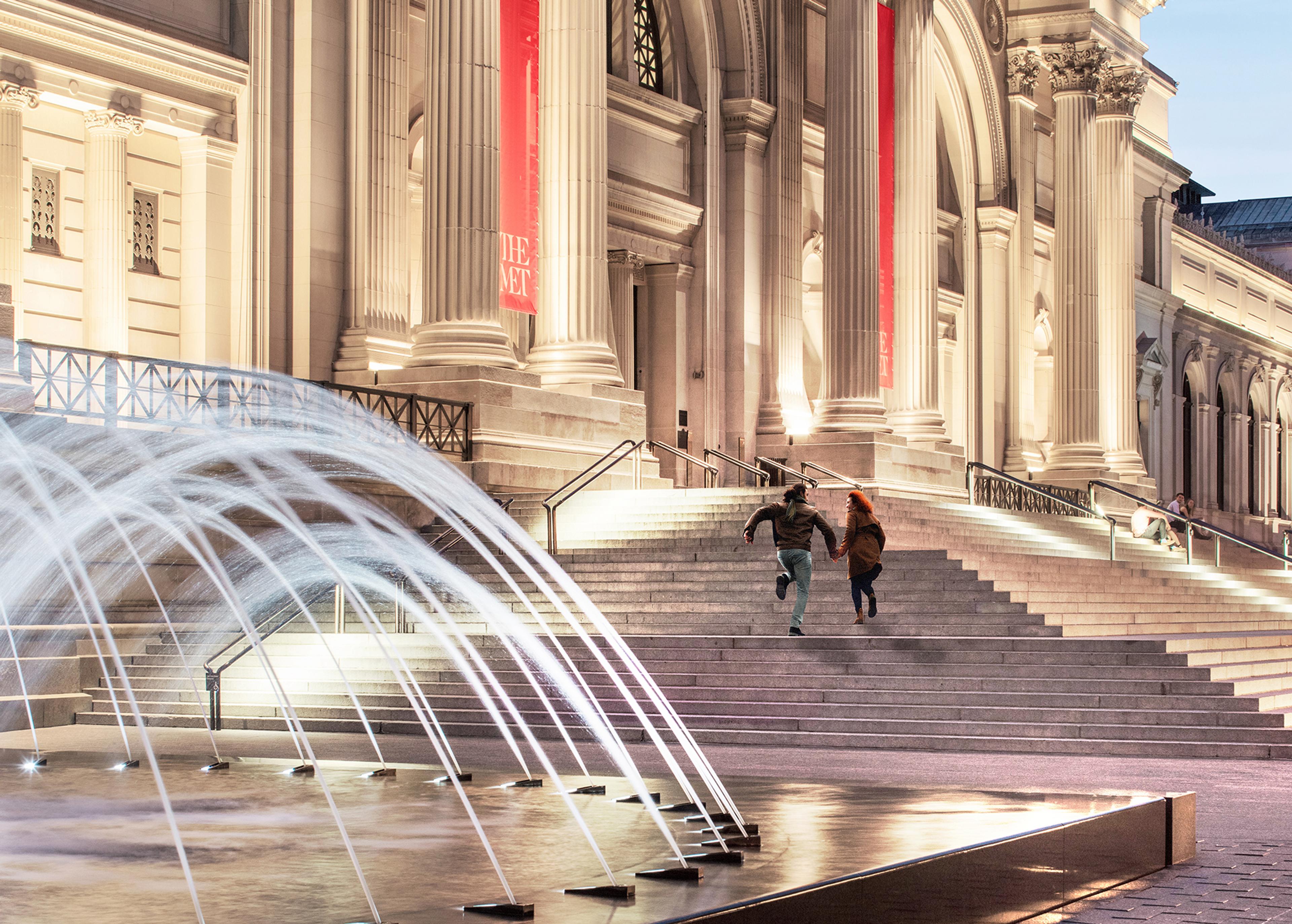 Two people run up The Met Steps at dusk.