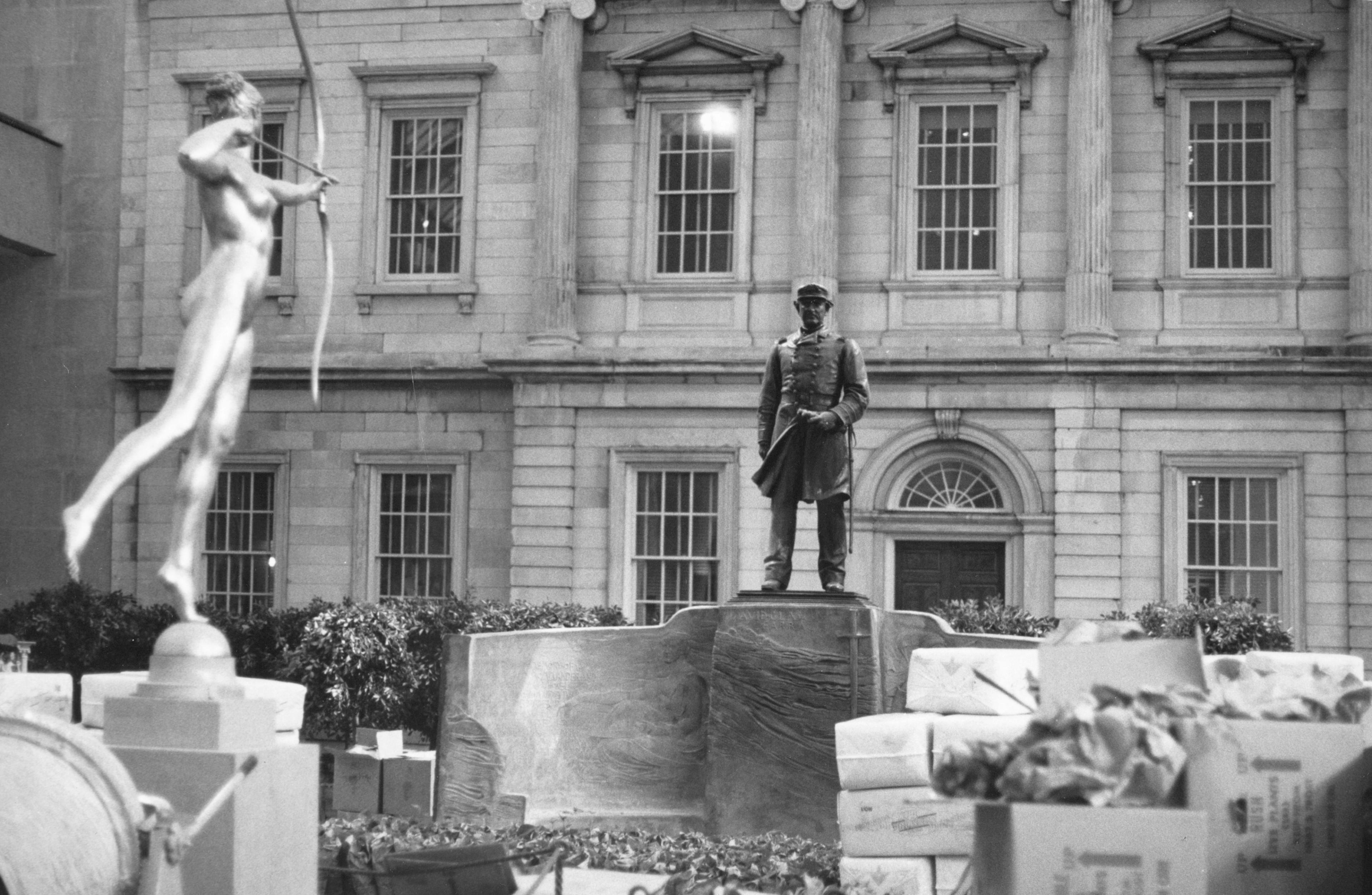 Archival, black-and-white photo showing Diana and a sculpture of a solider against a stoic building facade.