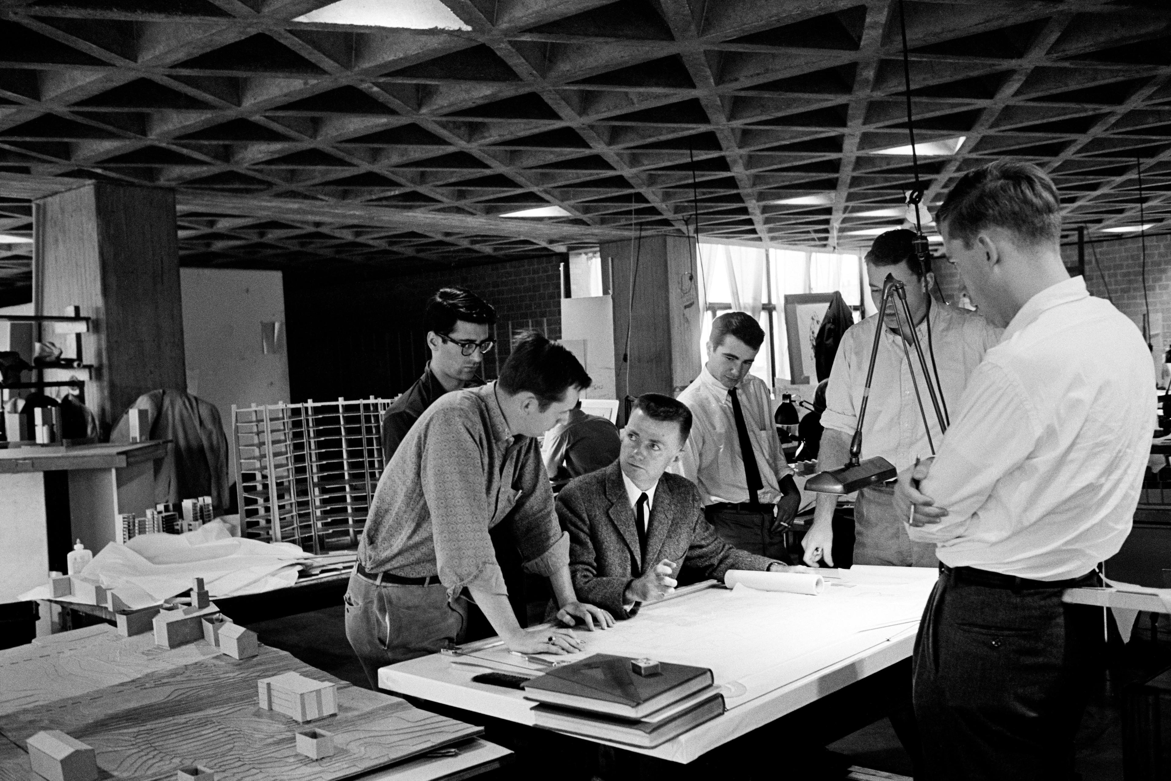 Men gathered around a table over sketched and blueprints