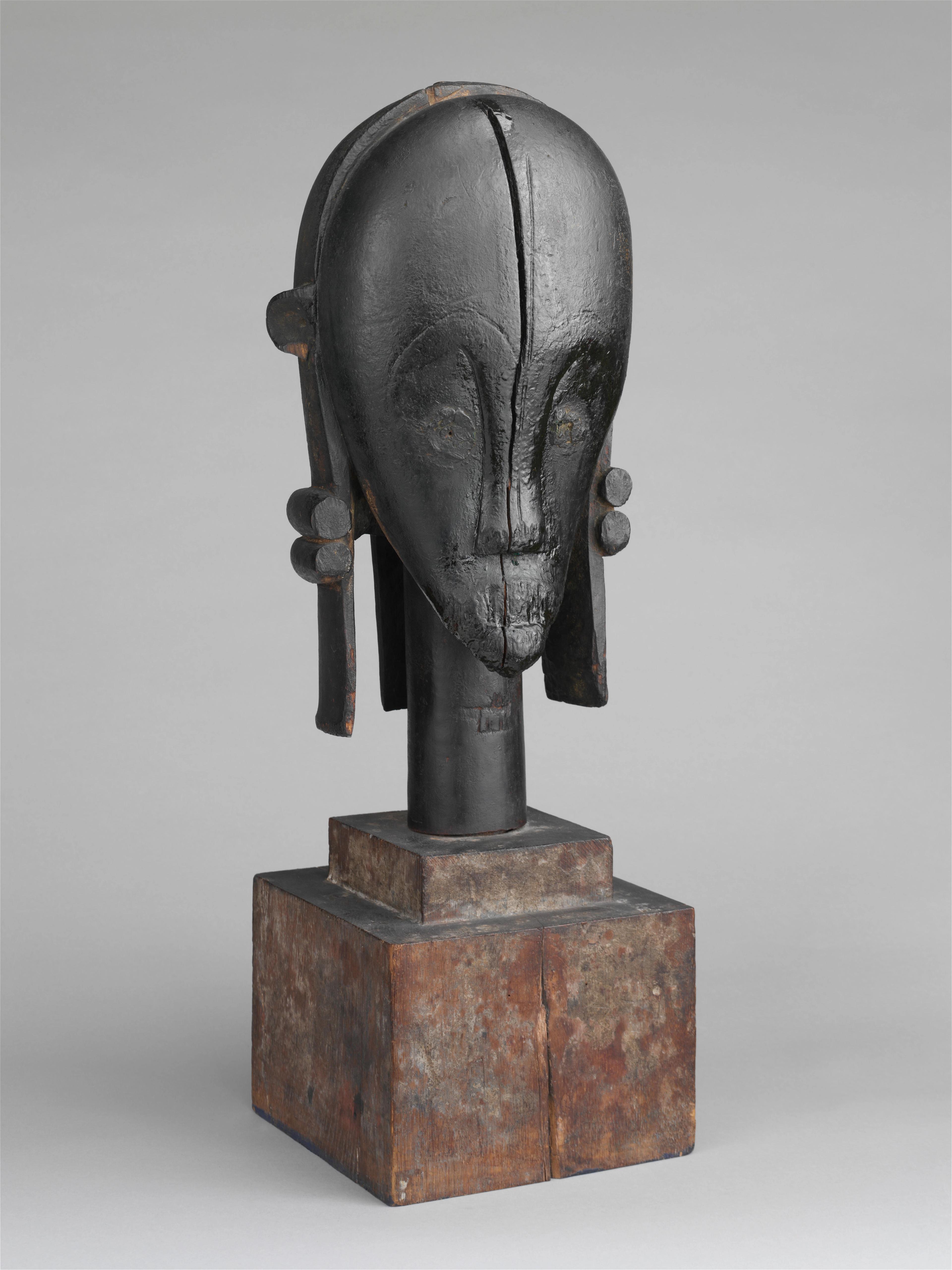 Sculpture in black wood of a head with a domed forehead, narrow chin, and decorative bands of hair.