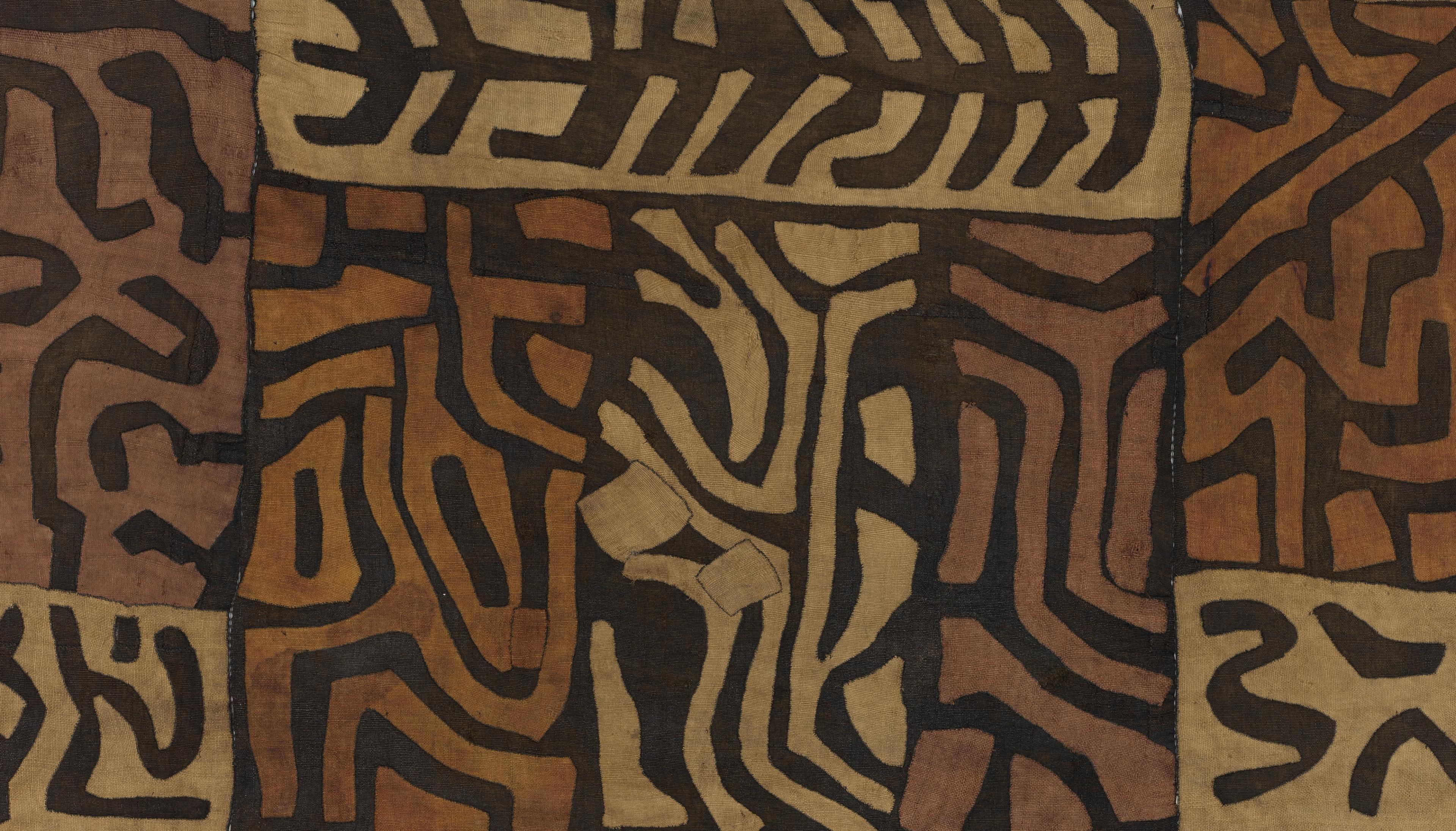 Detail of a fabric decorated with black geometric symbols arranged in sections across a brown and tan woven surface.