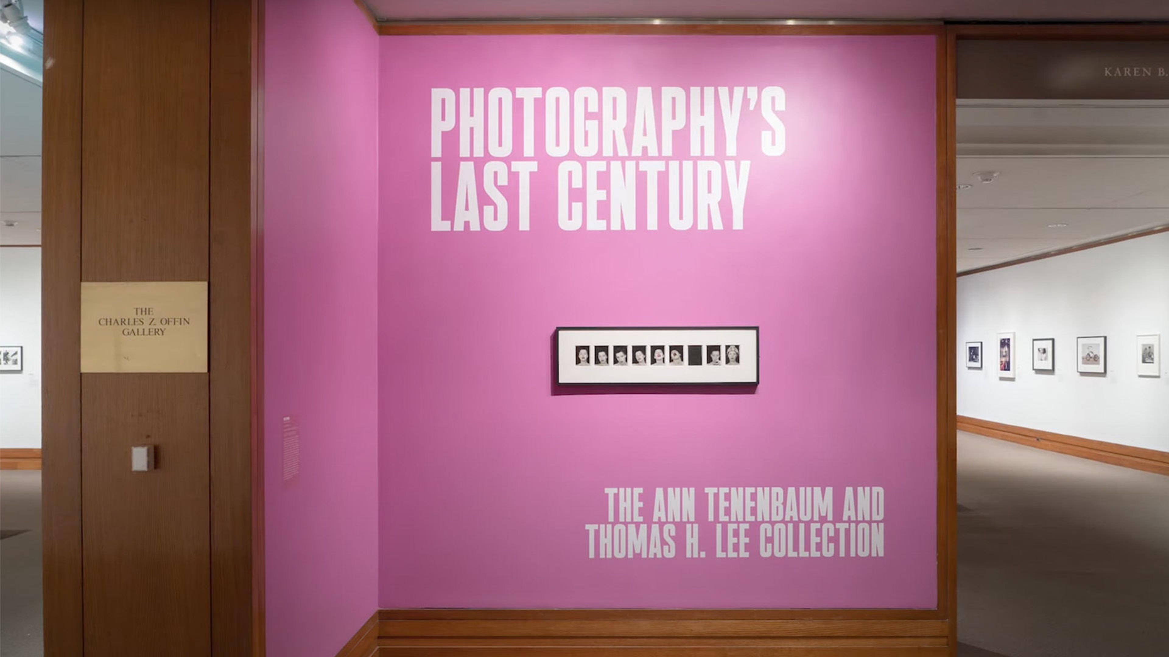 A sign on a pink wall reads Photography's last century. Below a nine framed heashots of the same person making different faces.