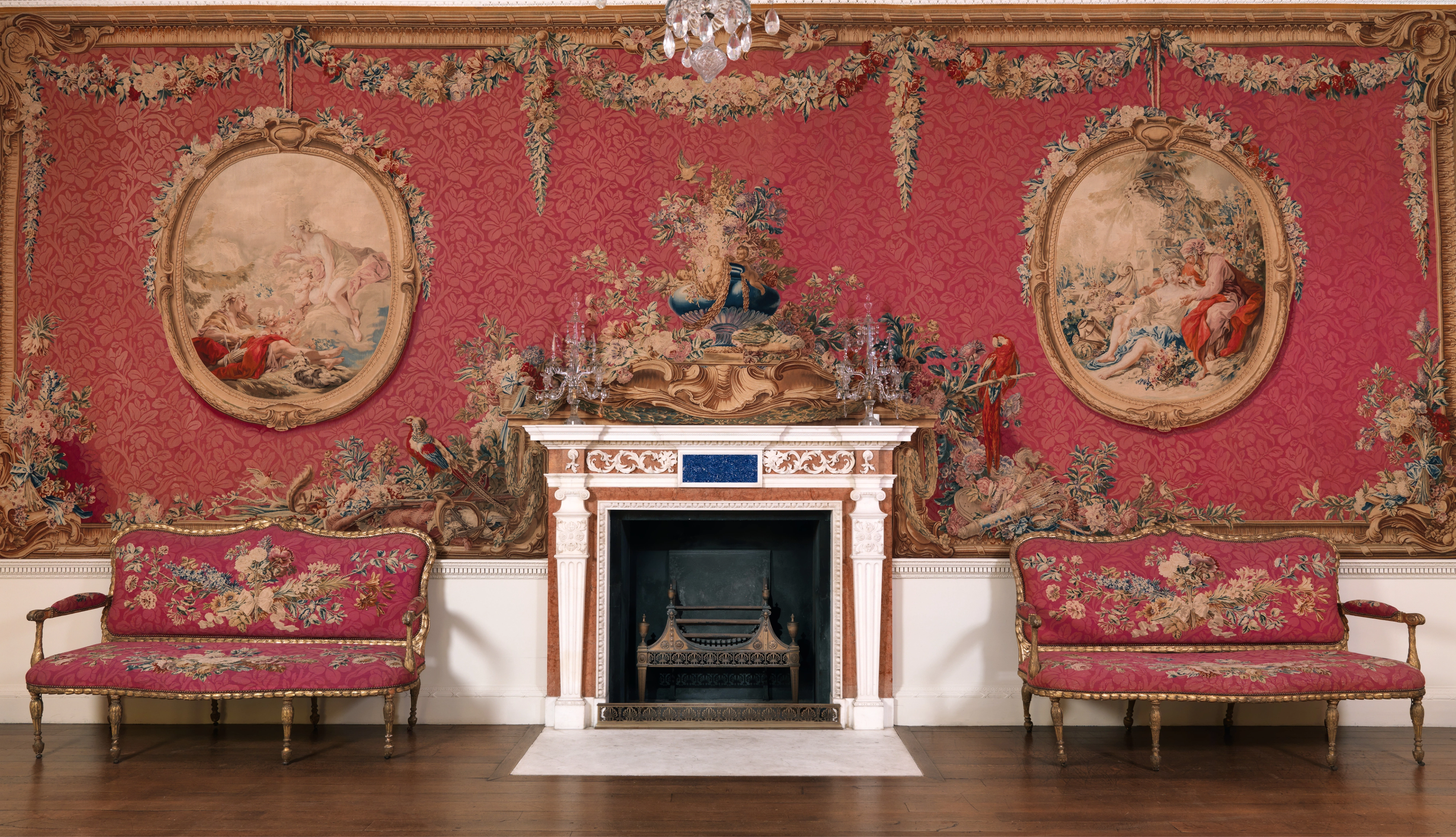 Tapestry room with a fireplace at the center, flanked by ornately decorated pink couches that match the large tapestry on the wall.