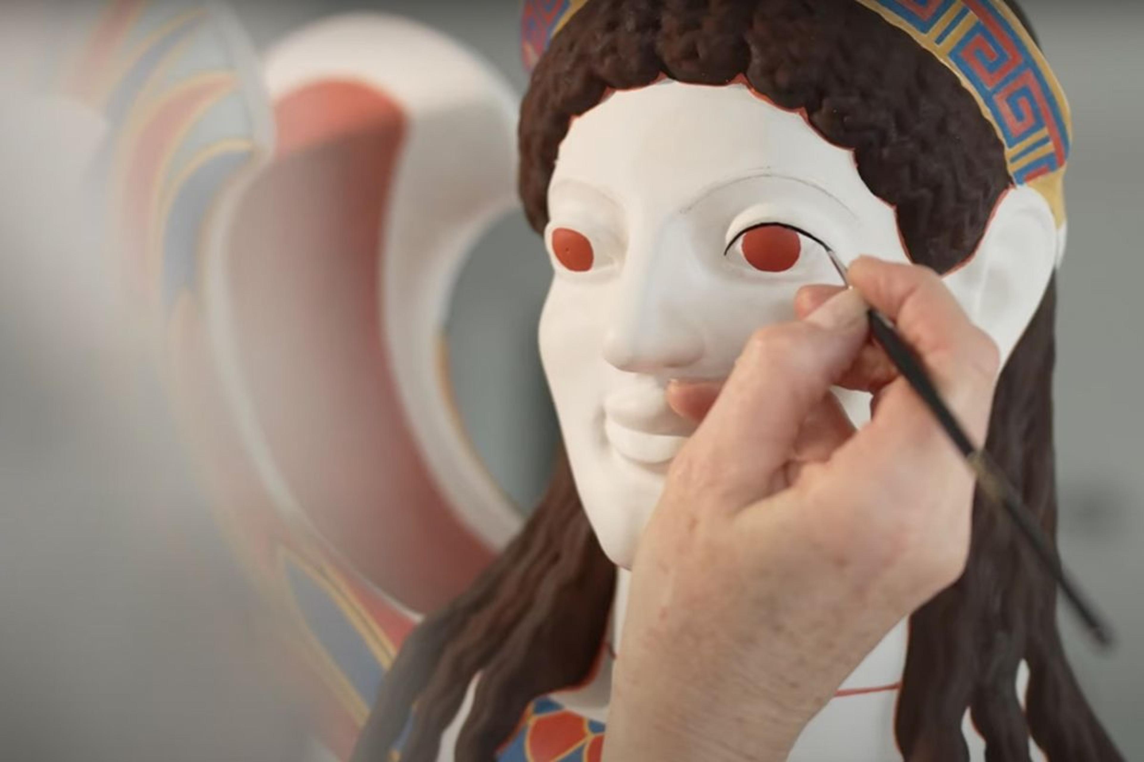 A light-skin-toned hand works to paint an eye detail on a model of an ancient greek sculpture.