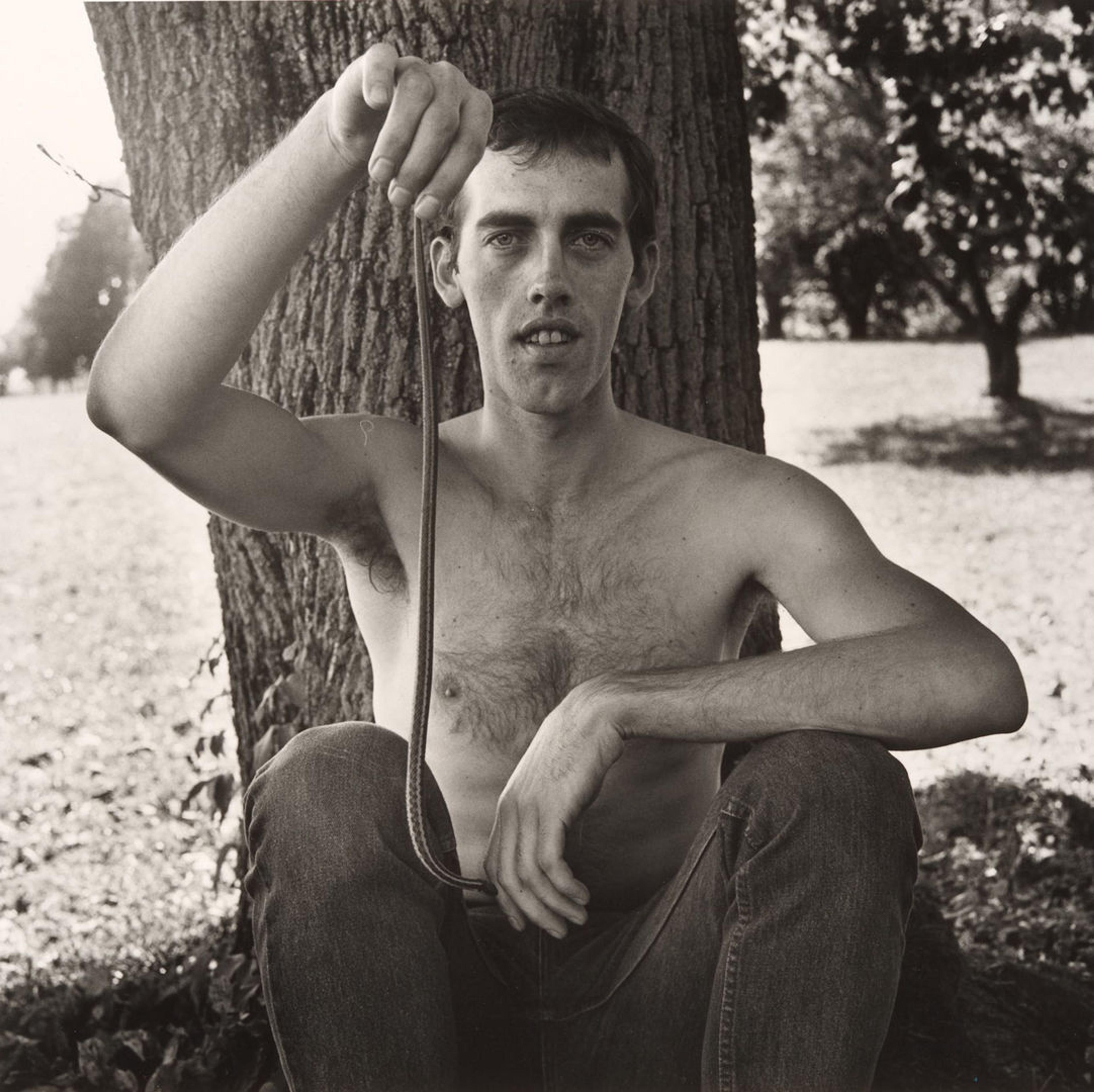 A portrait by Peter Hujar of fellow artist David Wojnarowicz holding a snake in a pastoral scene