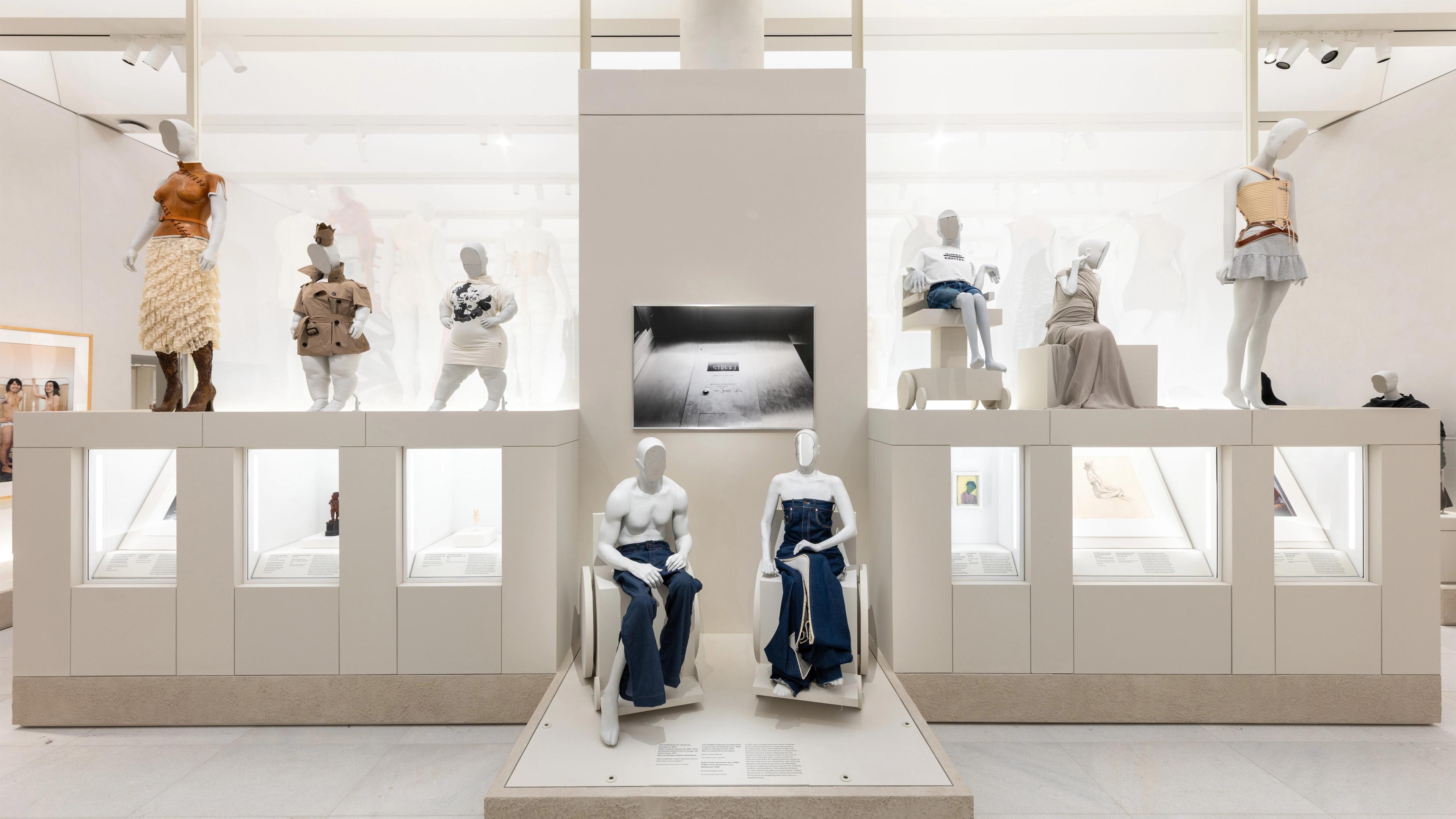 Museum display of modern fashion features mannequins wearing innovative textile art. Neutral tones and dynamic silhouettes.