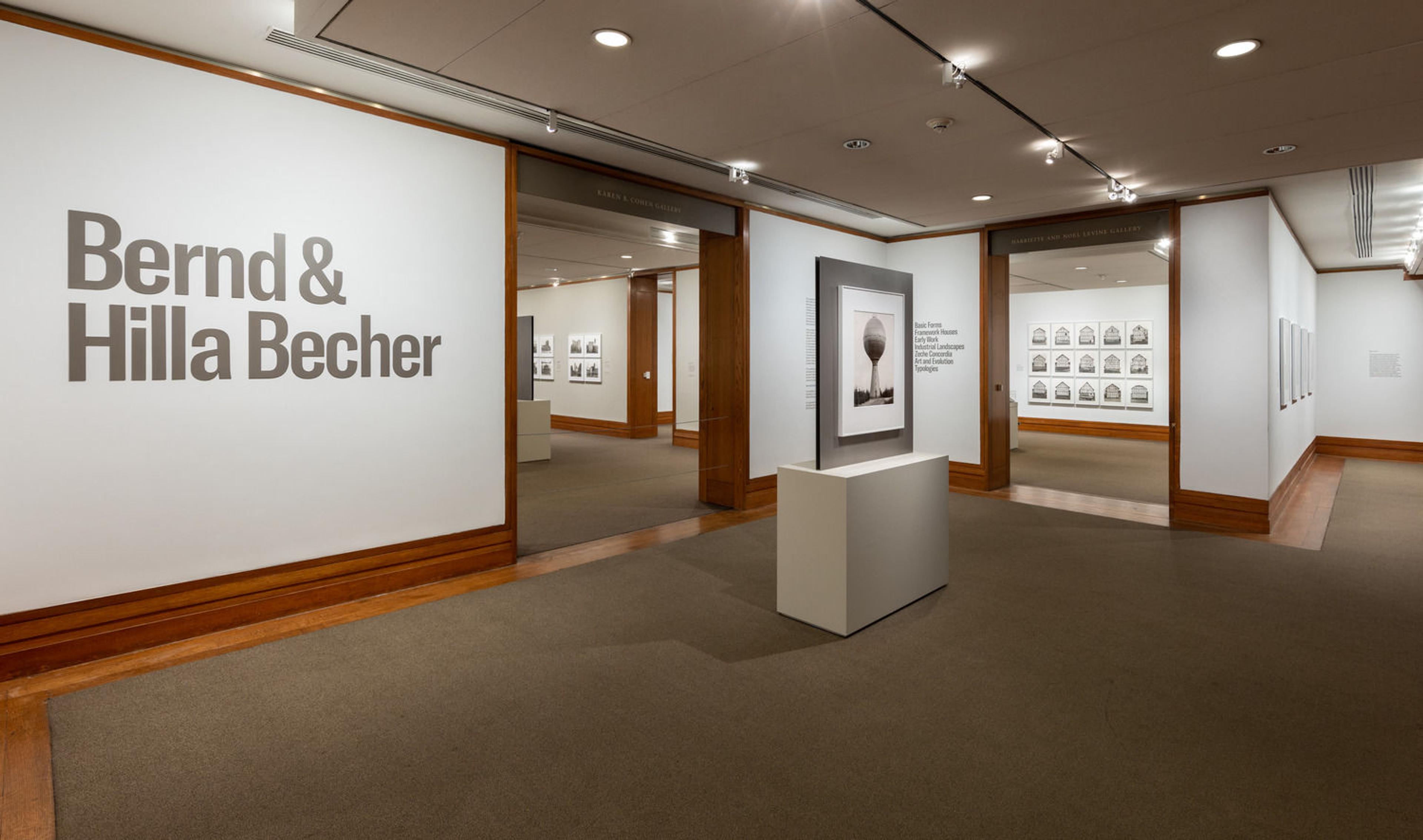 Photograph of gallery space with photographs, wood panelling, and "Bernd & Hilla Becher" printed on the wall.