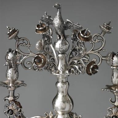 An ornate silver menorah with flowers, birds, and lions