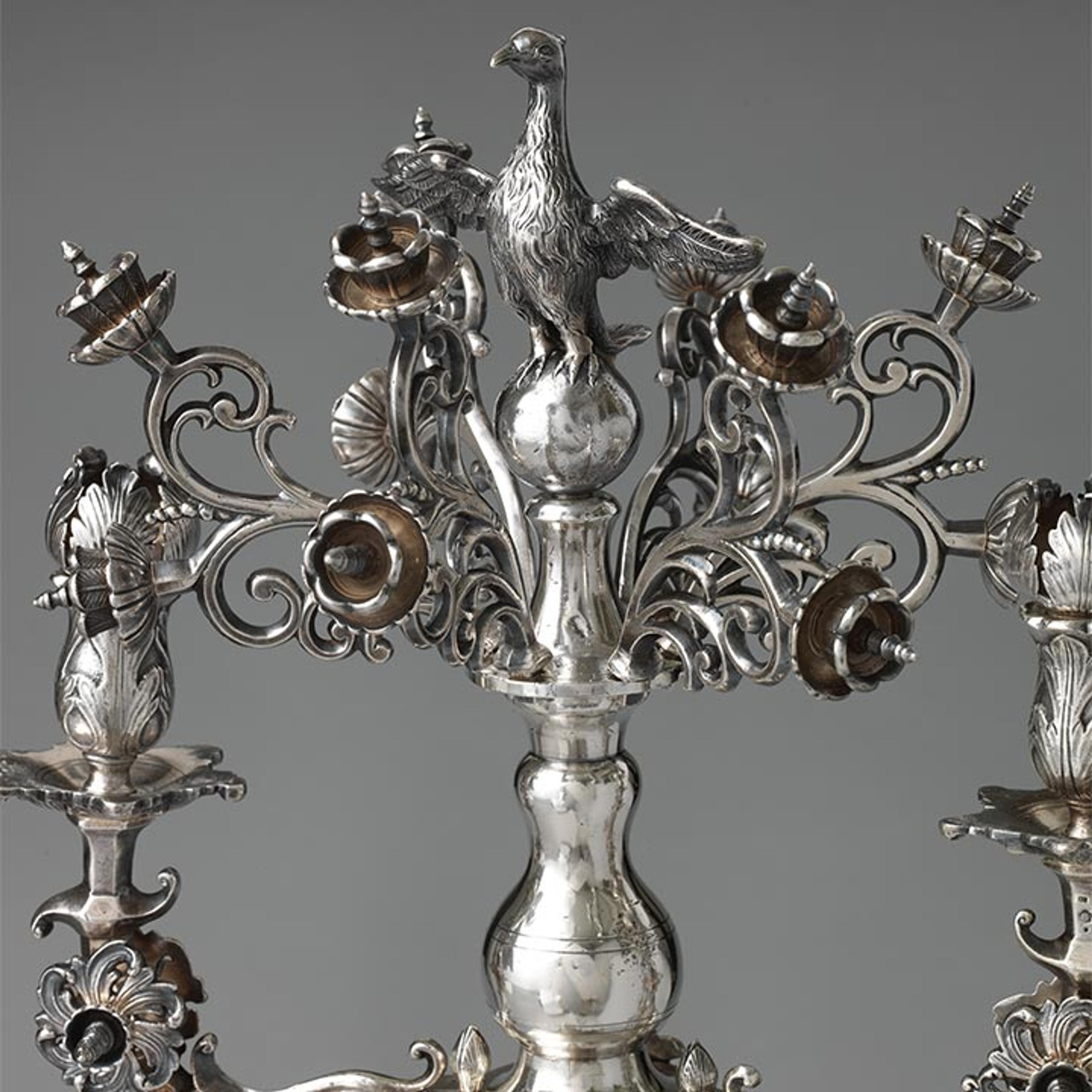 An ornate silver menorah with flowers, birds, and lions