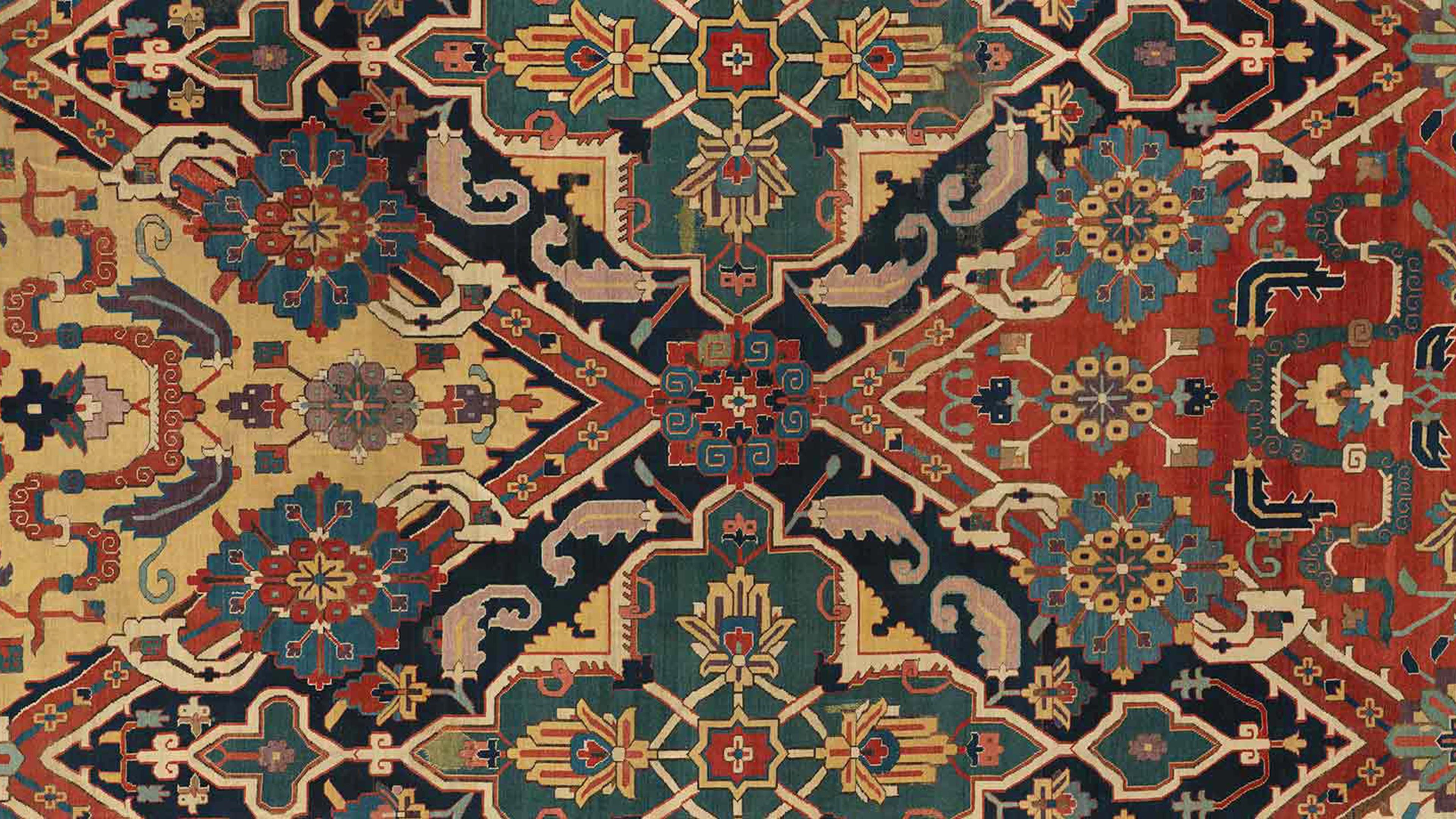 A richly colored, symmetrical rug with intricate geometric and floral patterns in shades of red, blue, green, beige, and gold.