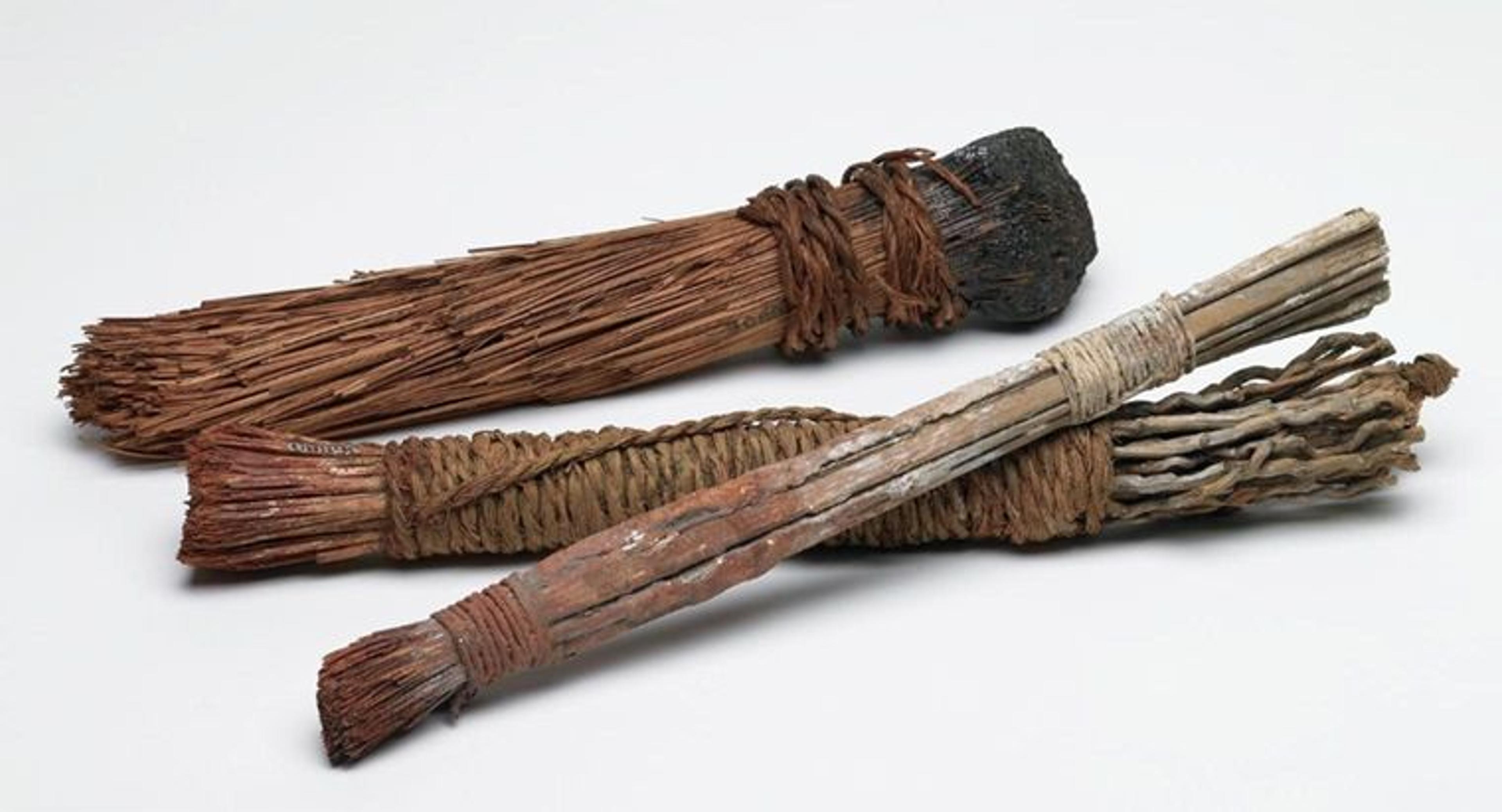 Three ancient Egyptian paint brushes against a white background.