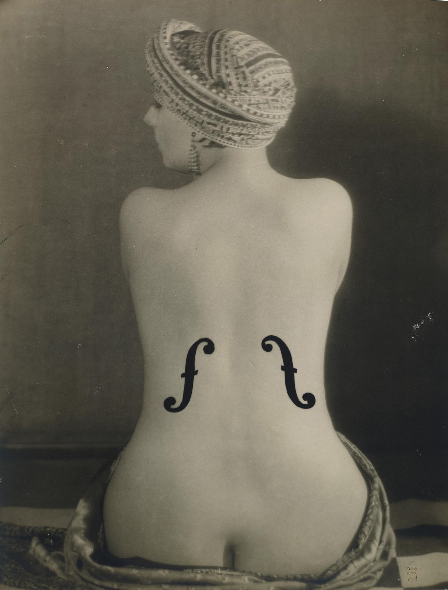 Back view of a nude woman with a turban, posed to resemble a violin with f-holes painted on her back. The image conveys elegance and creativity.