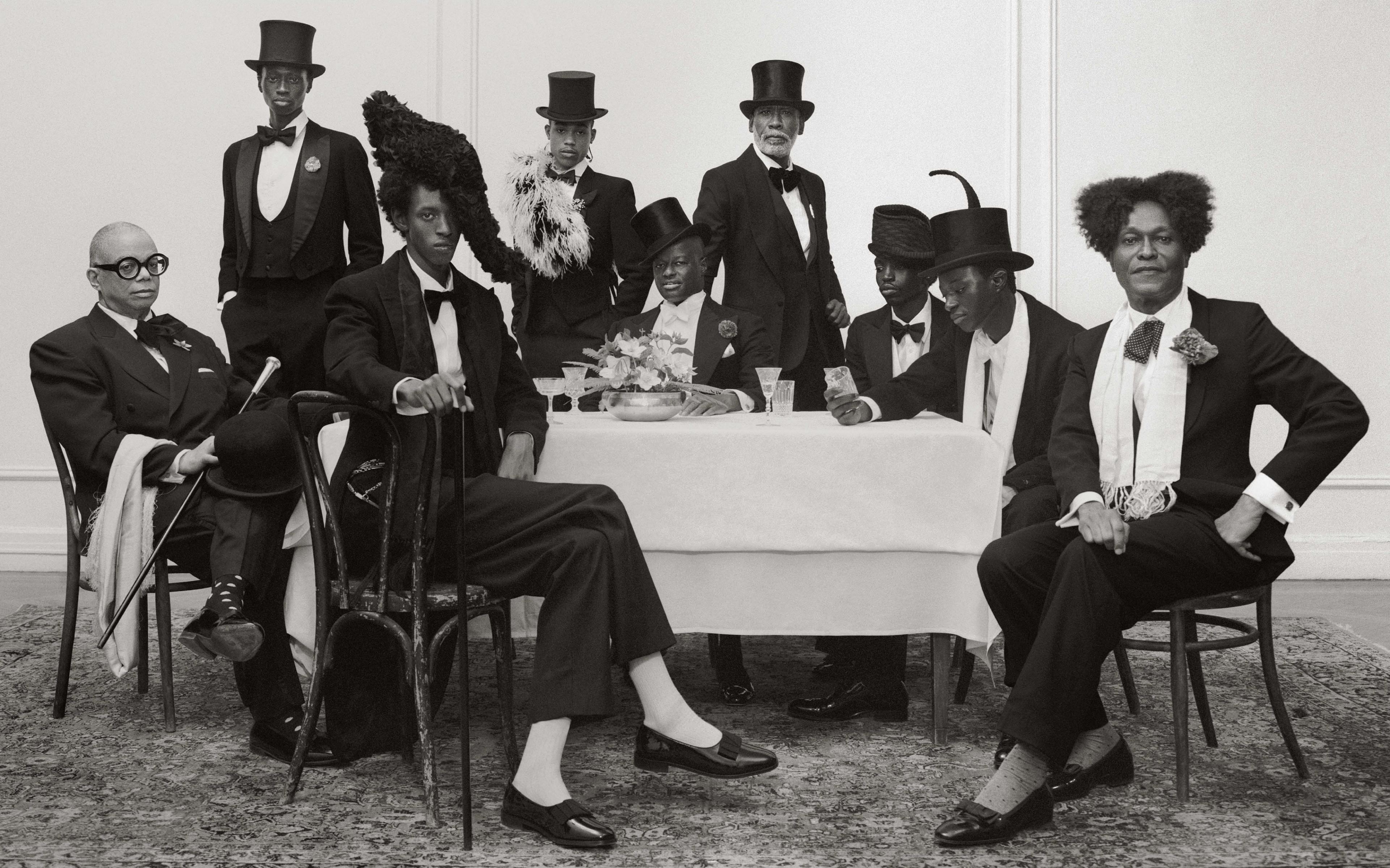 Black-and-white photograph of a group of men wearing tuxedos and elaborate, whimsical hats