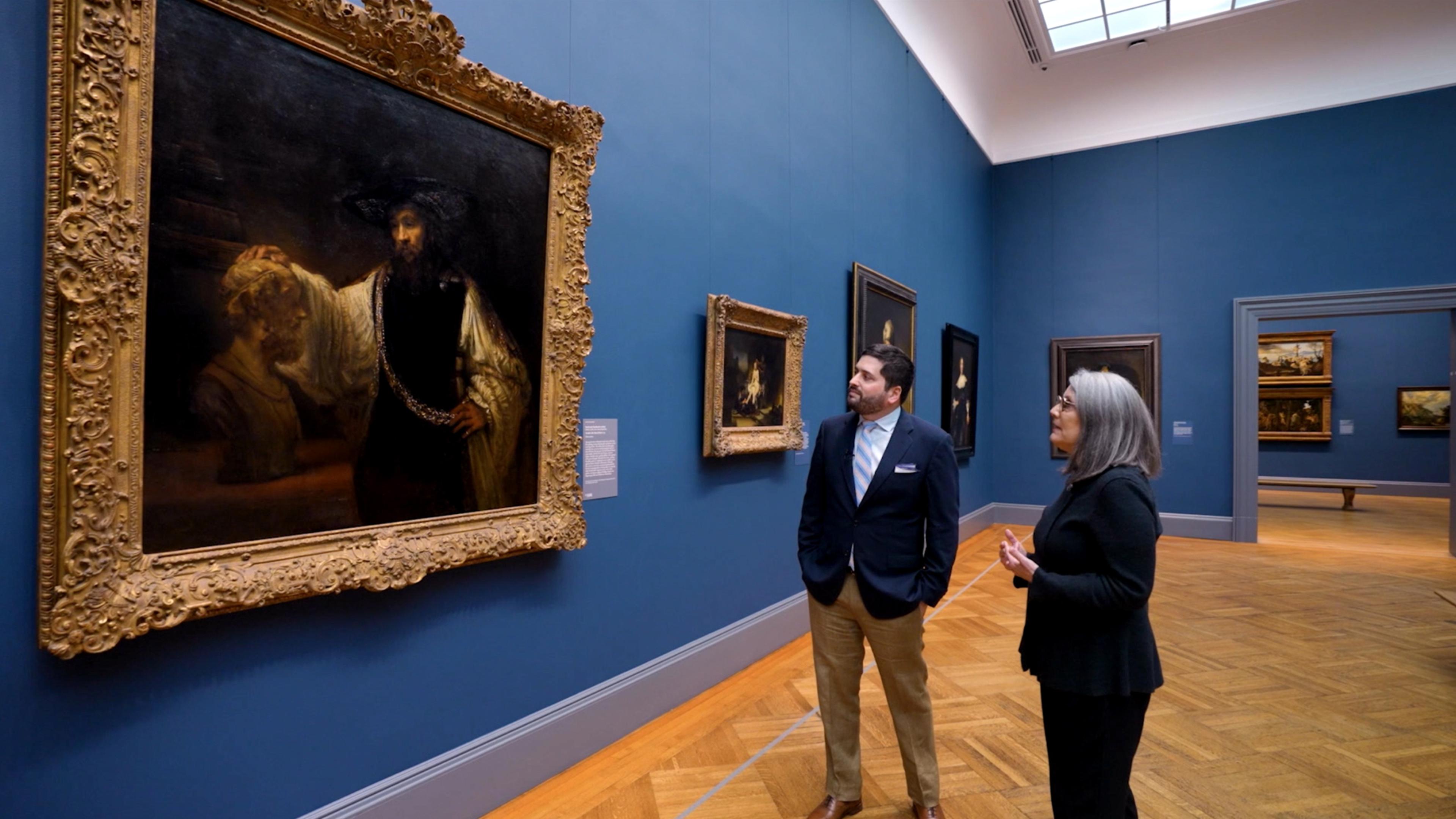 Two people standing in the European Paintings galleries looking at a painting
