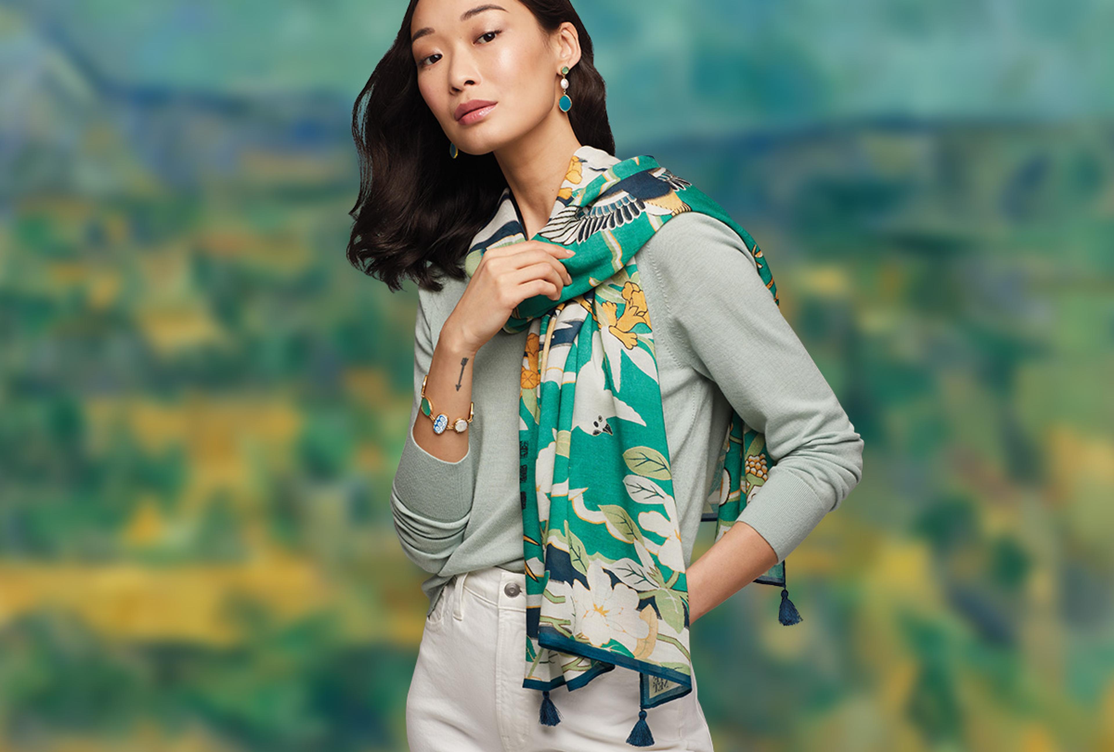 A young Asian woman models a green printed scarf against a green and blue blurred background.