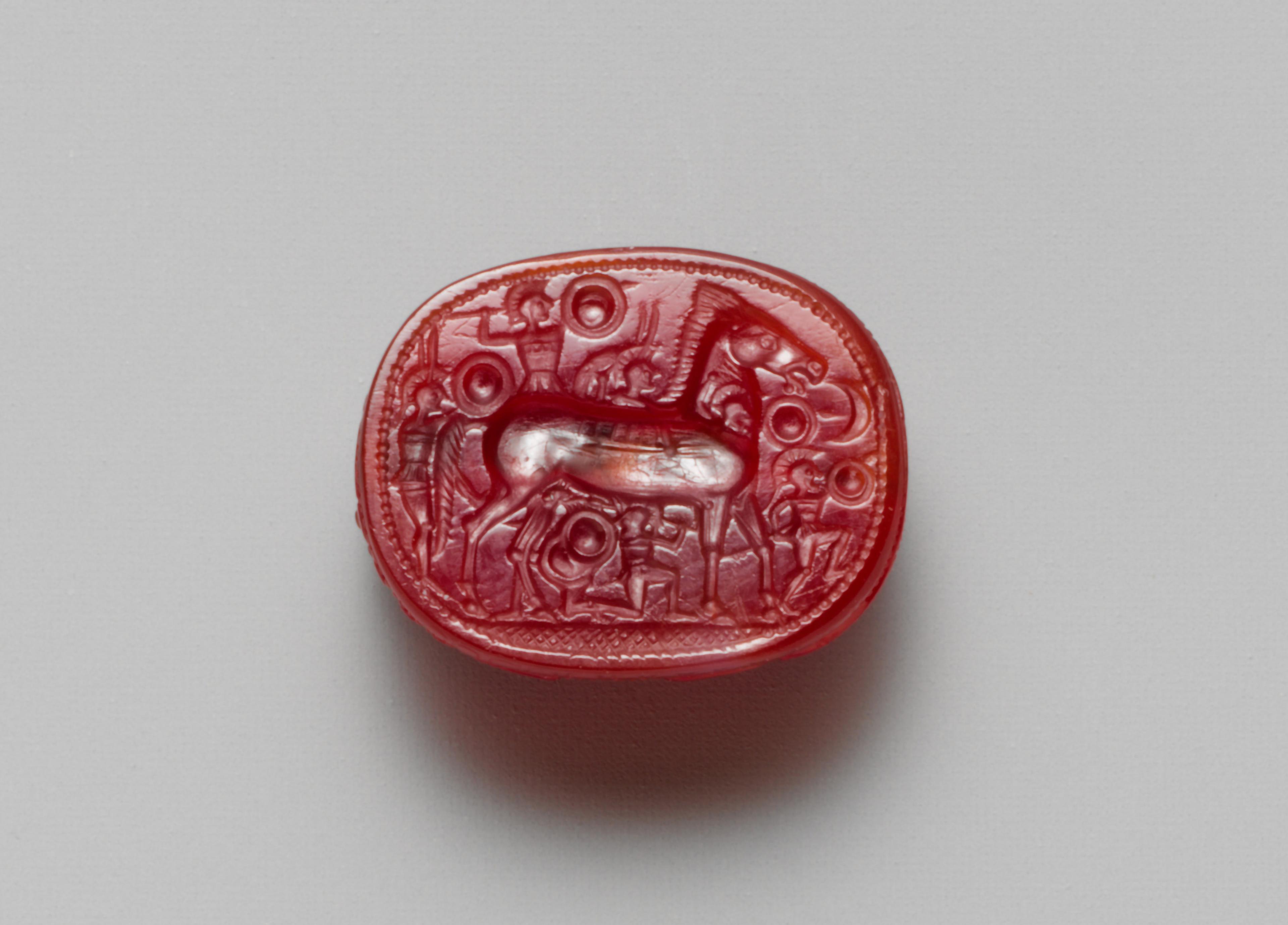 Small red stone, intricately carved with a horse and shield-wielding fighters.