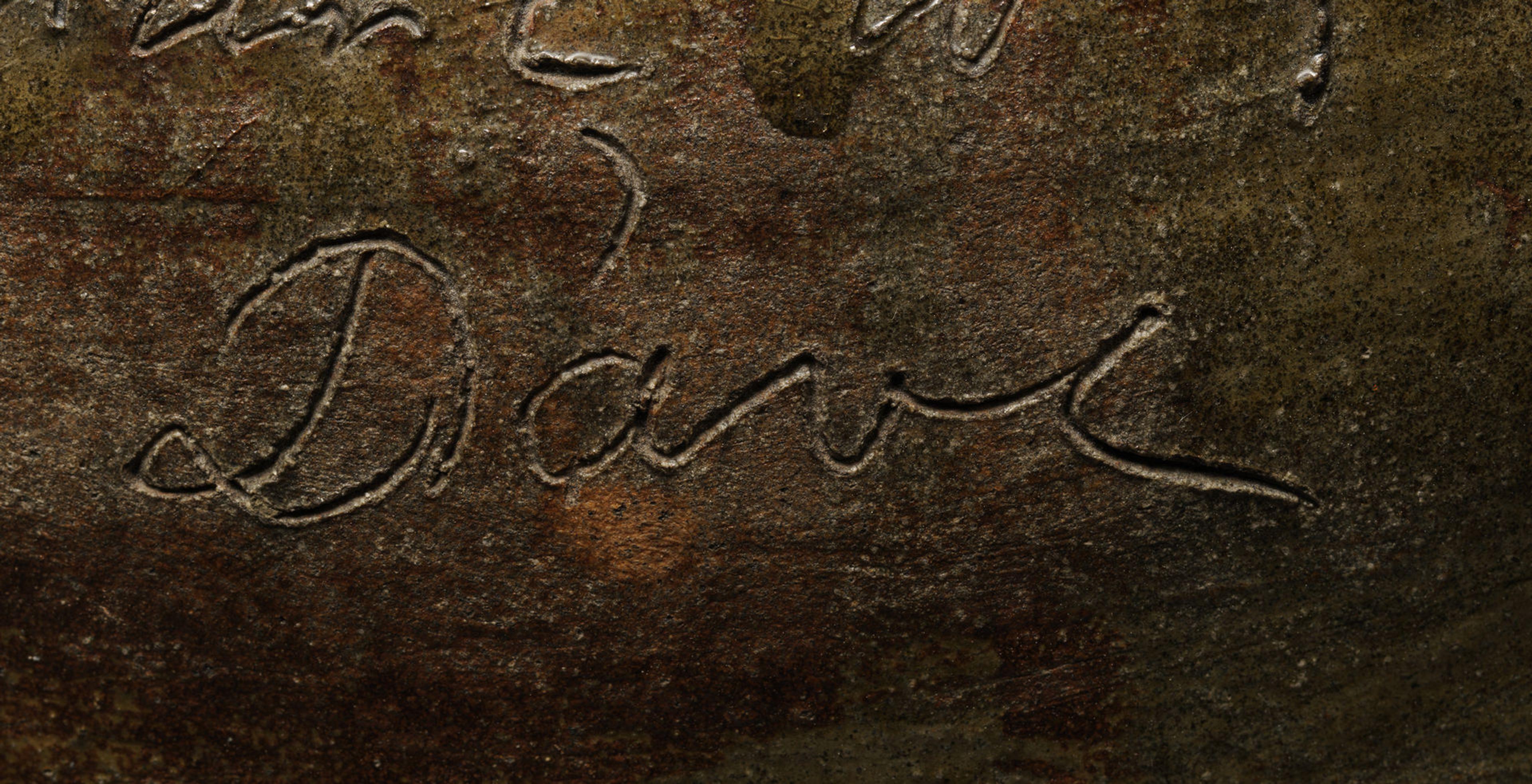 Closeup of a handwritten name, "Dave," engraved onto a brown and yellow stone surface.