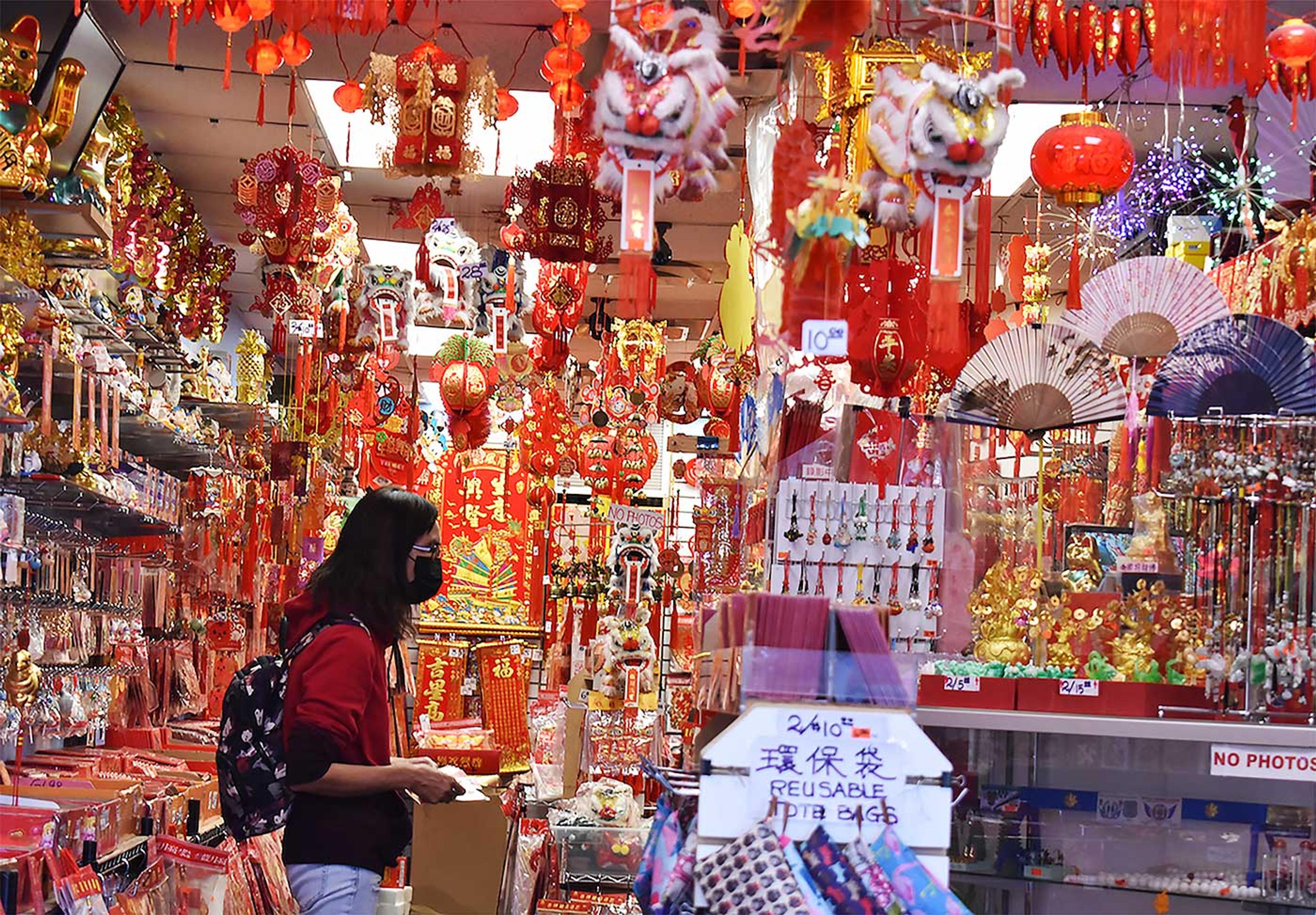 Photograph of a woman standing inside a shop surrounded by Chinese New Year decorations.