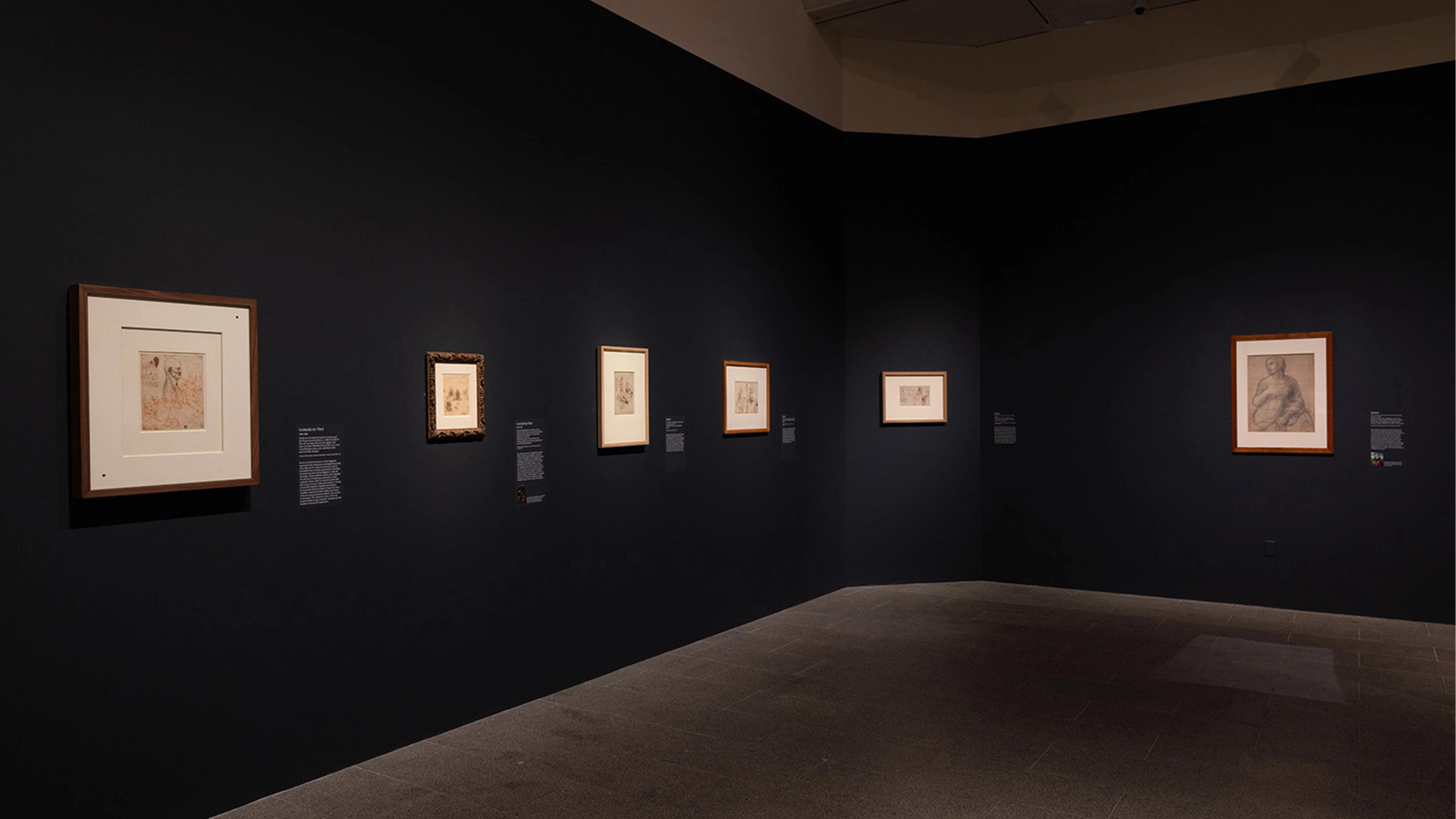 Dimly lit art gallery with a dark blue wall showcasing six framed sketches.