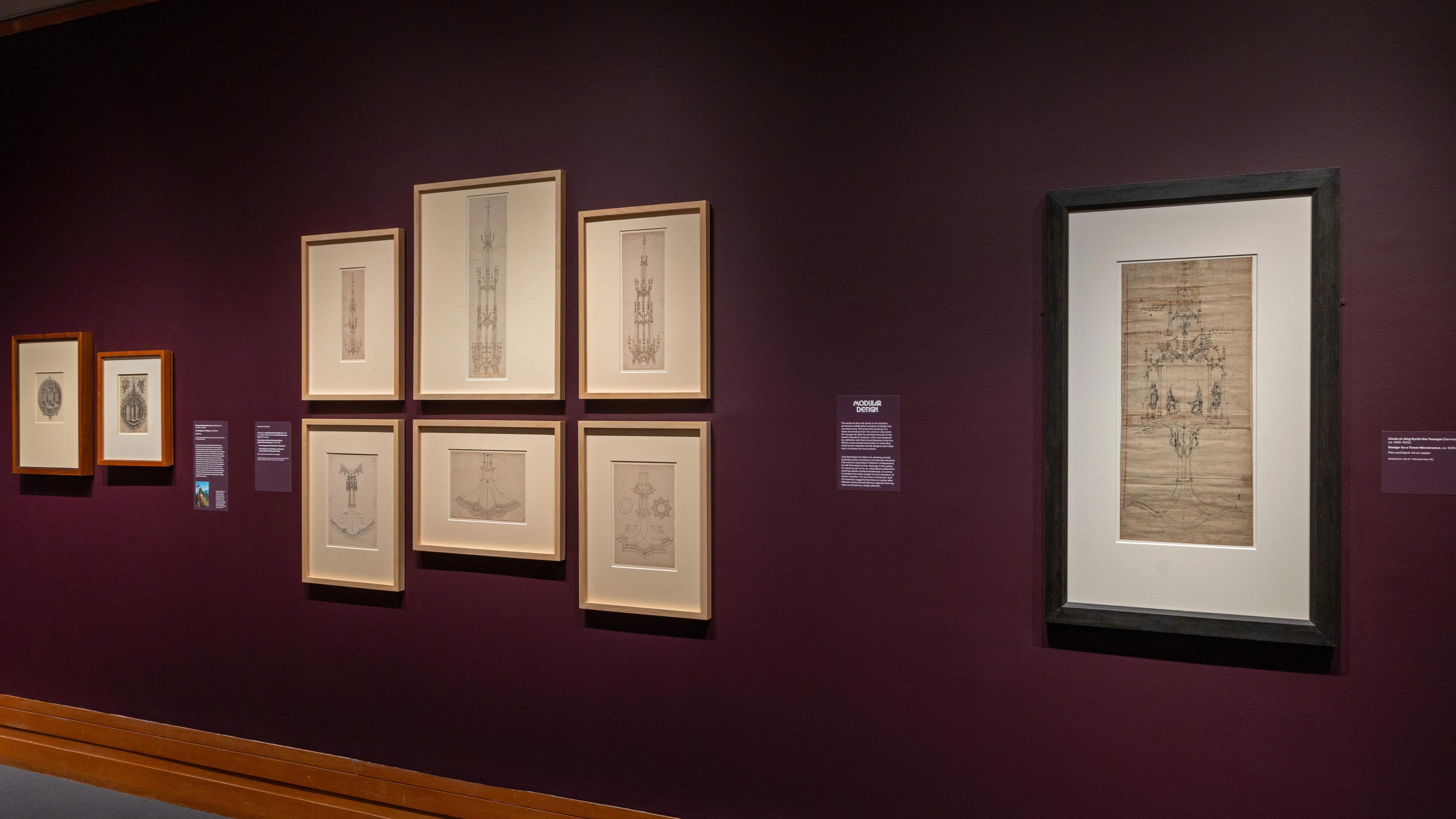 Exhibition wall with framed sketches on a deep purple background.