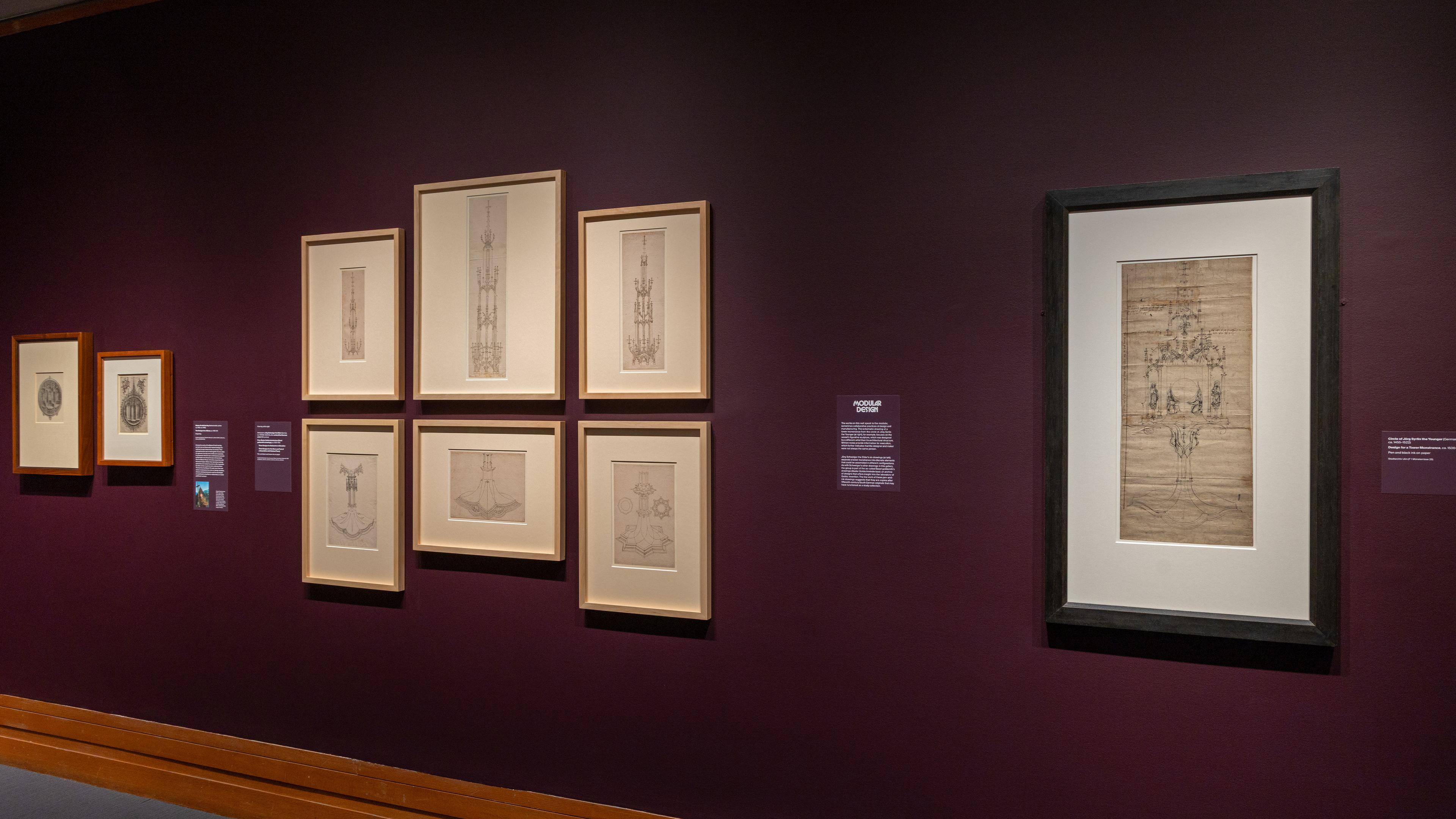 Exhibition wall with framed sketches on a deep purple background.