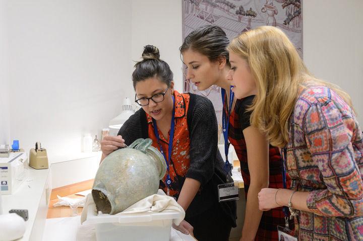 Two students and a conservator take a close look at a ceramic urn