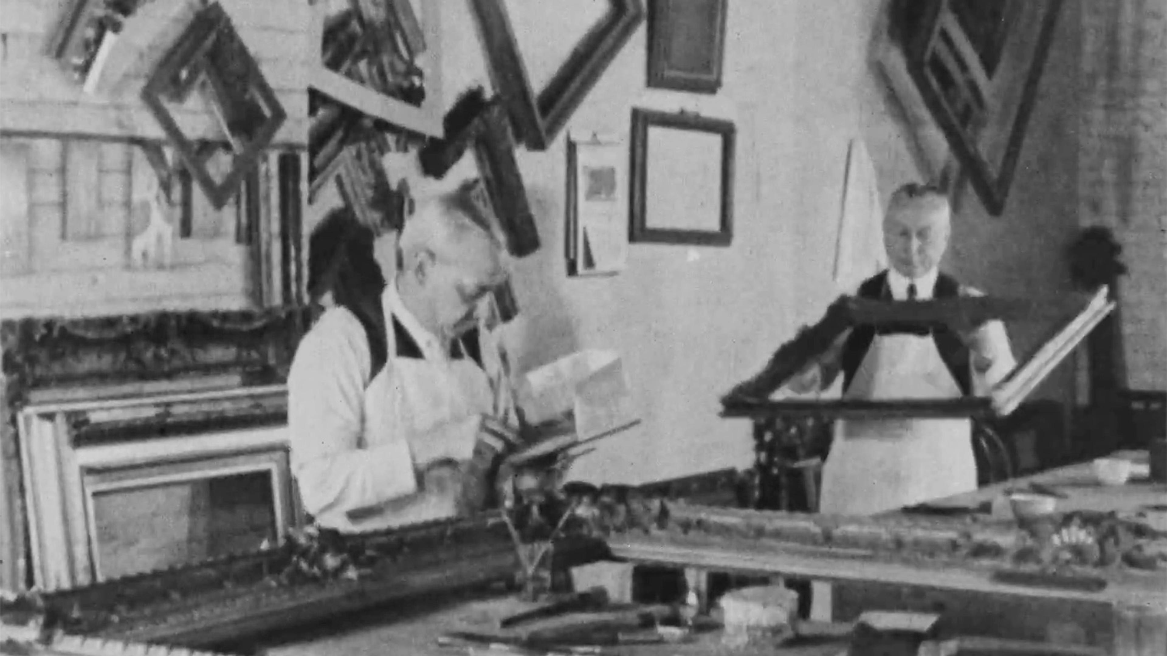 Black-and-white photo of two men working with picture frames.