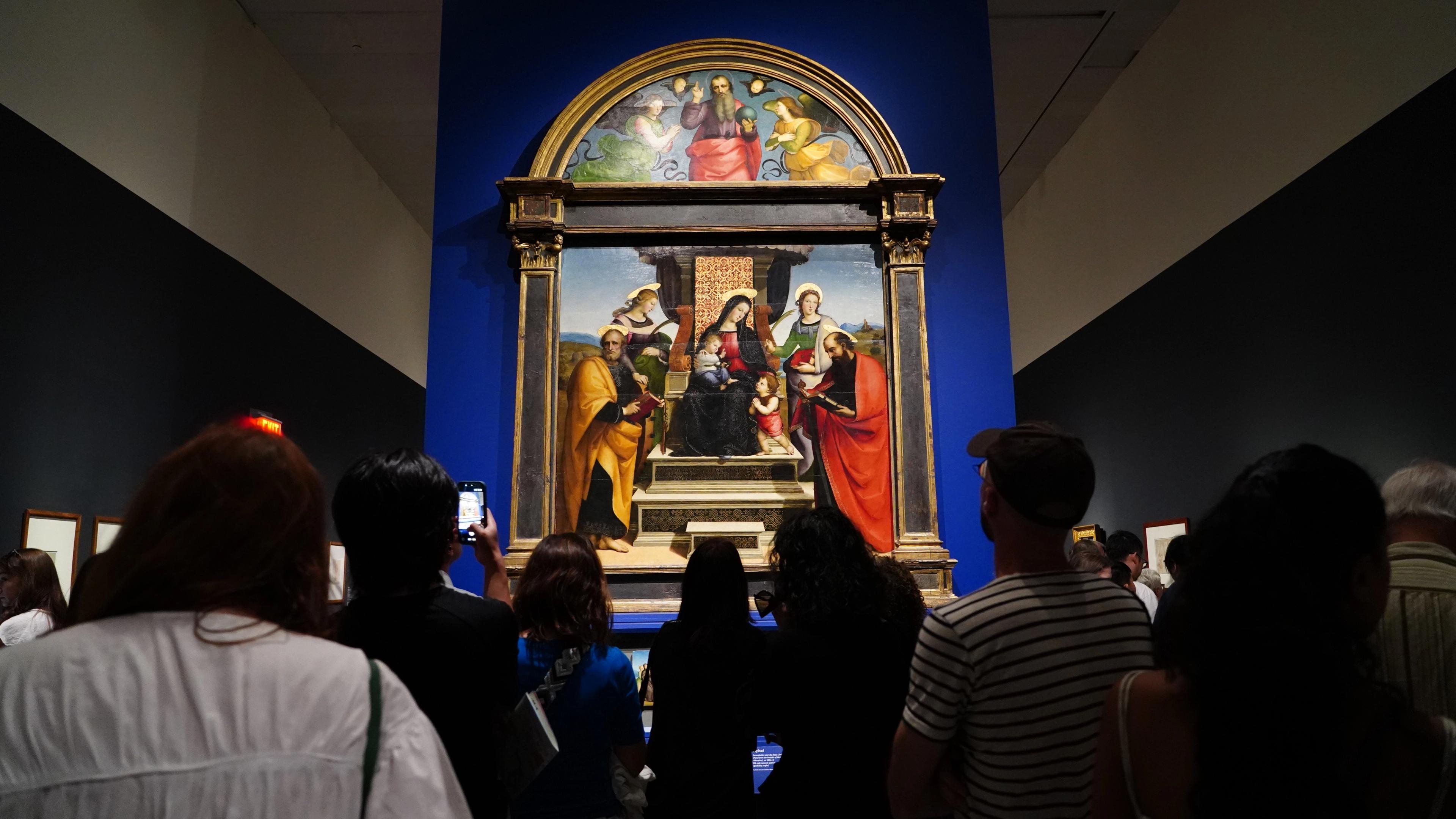 A gallery full of people looking at a religious altarpiece with the baby Jesus and Madonna