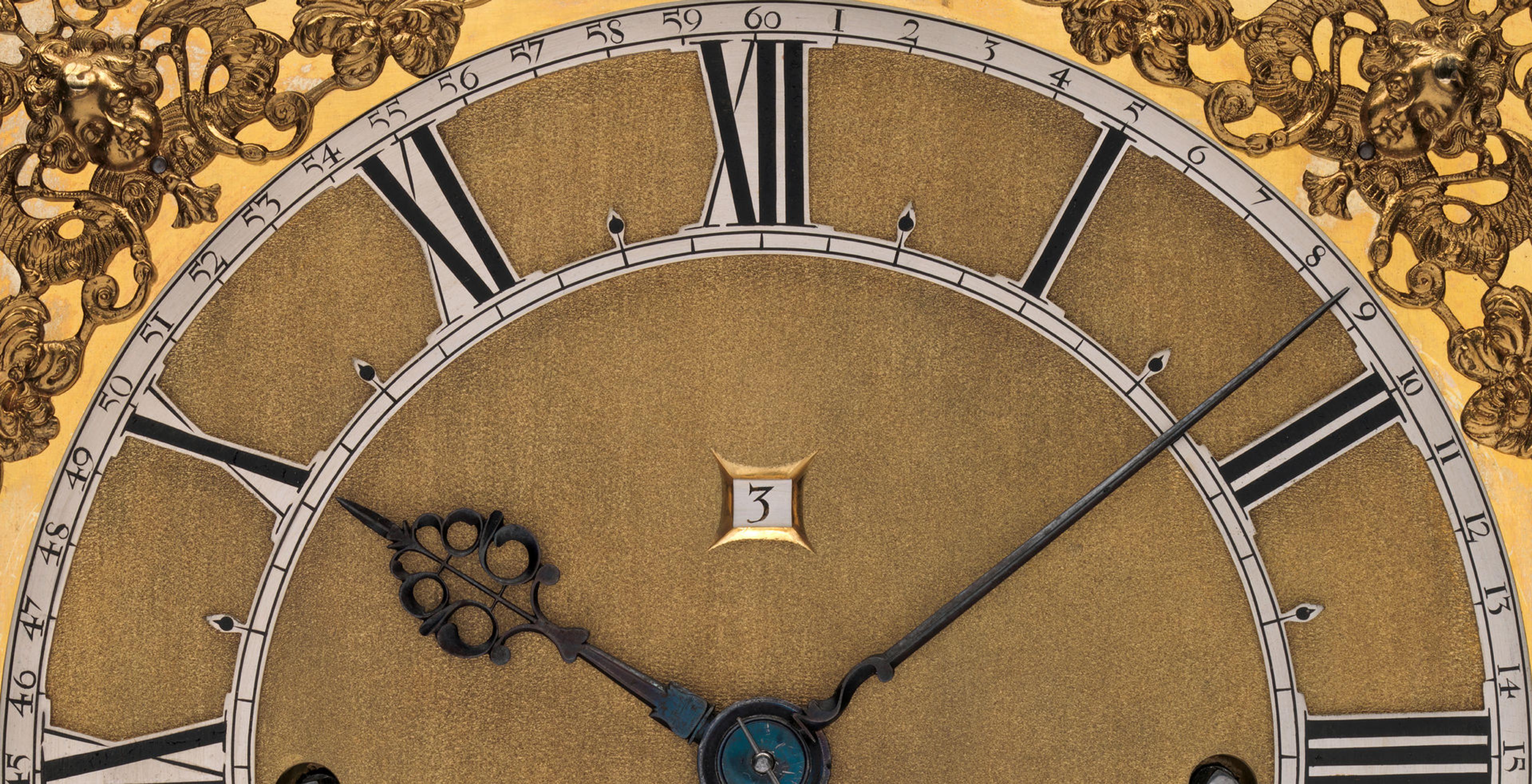 Detail of a clock face with gold-colored accents, roman numeral numbers, and a counter for the date.